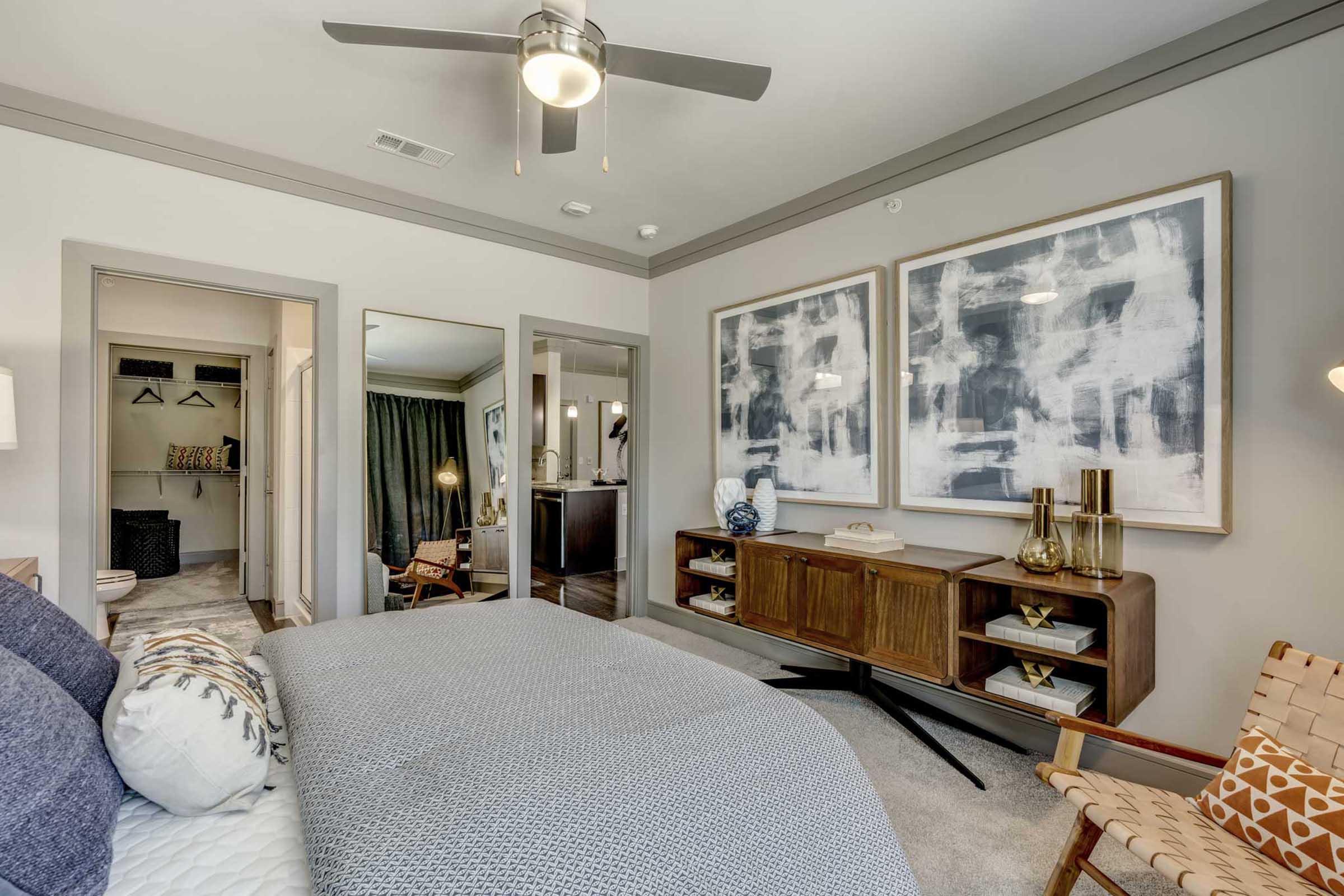 A modern bedroom featuring a king-sized bed with blue and gray bedding, a ceiling fan, and large artwork on the walls.