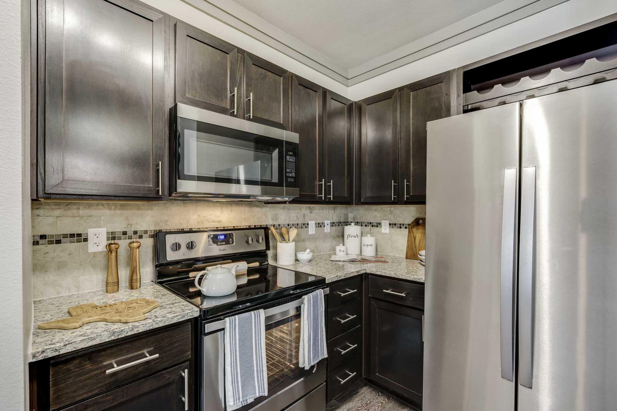 A modern kitchen featuring dark cabinetry, stainless steel appliances, and granite countertops.