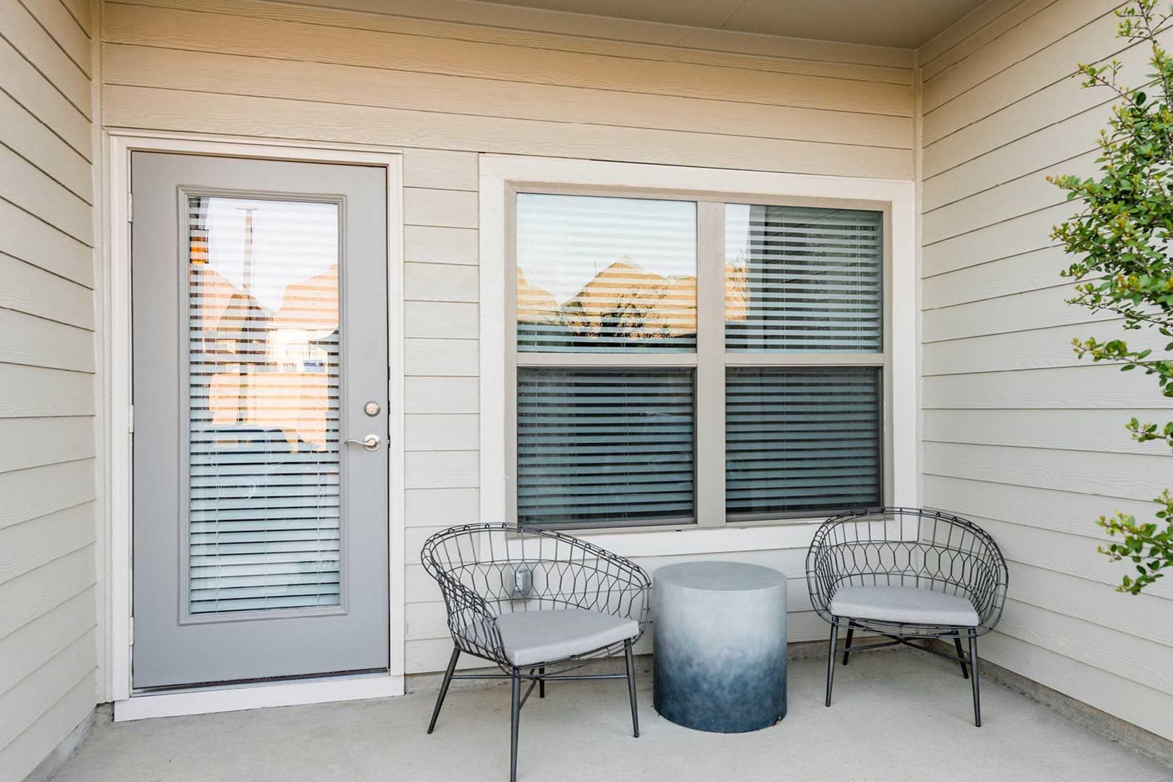 A cozy outdoor space featuring a sliding glass door, two modern wire chairs, and a round decorative table.