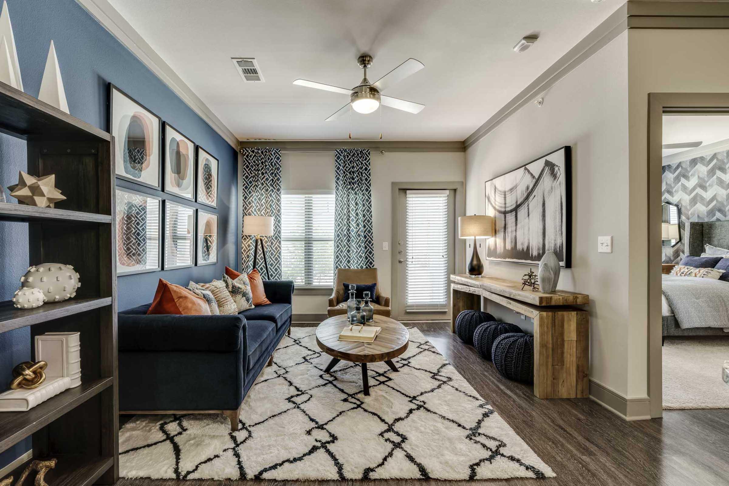 A modern living room featuring a navy blue sofa adorned with colorful cushions, a round wooden coffee table on a patterned rug, and a console table with decorative items.