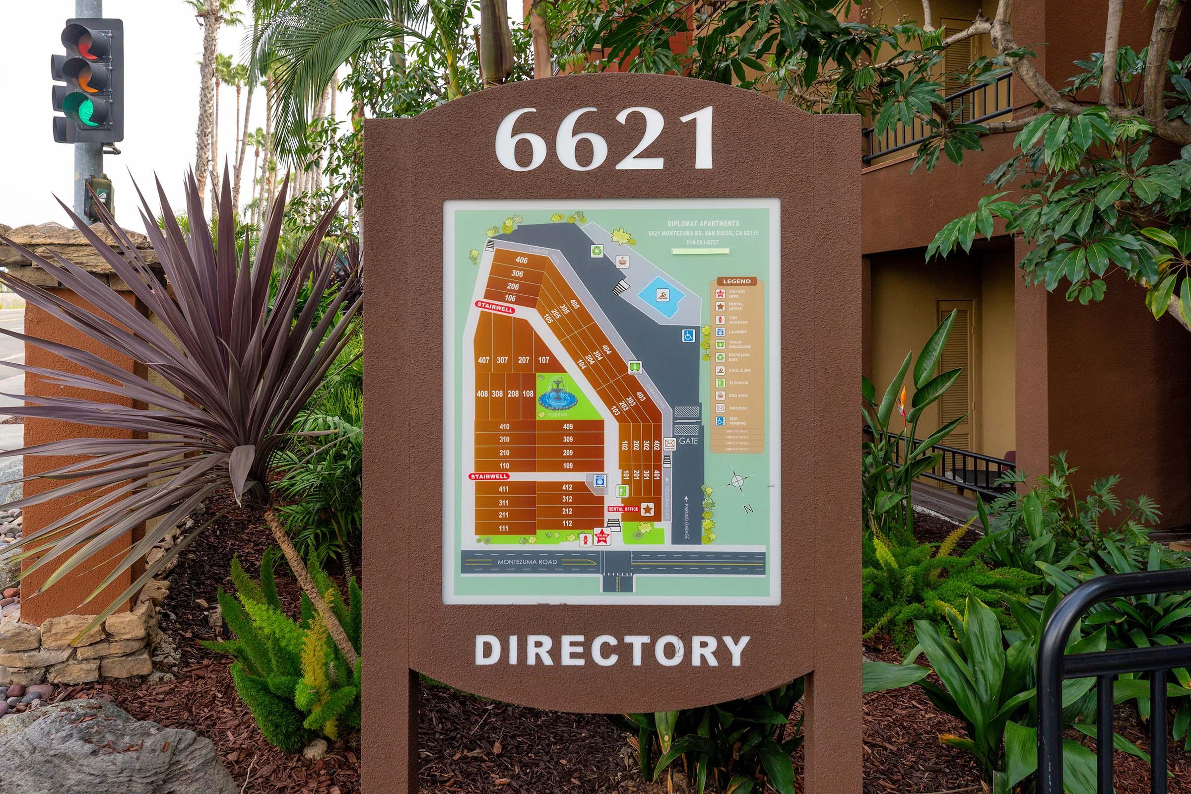 Directory map showing the layout of a property at 6621, with labeled sections, amenities, and nearby features. Surrounding the sign are various plants, and a traffic light in the background.