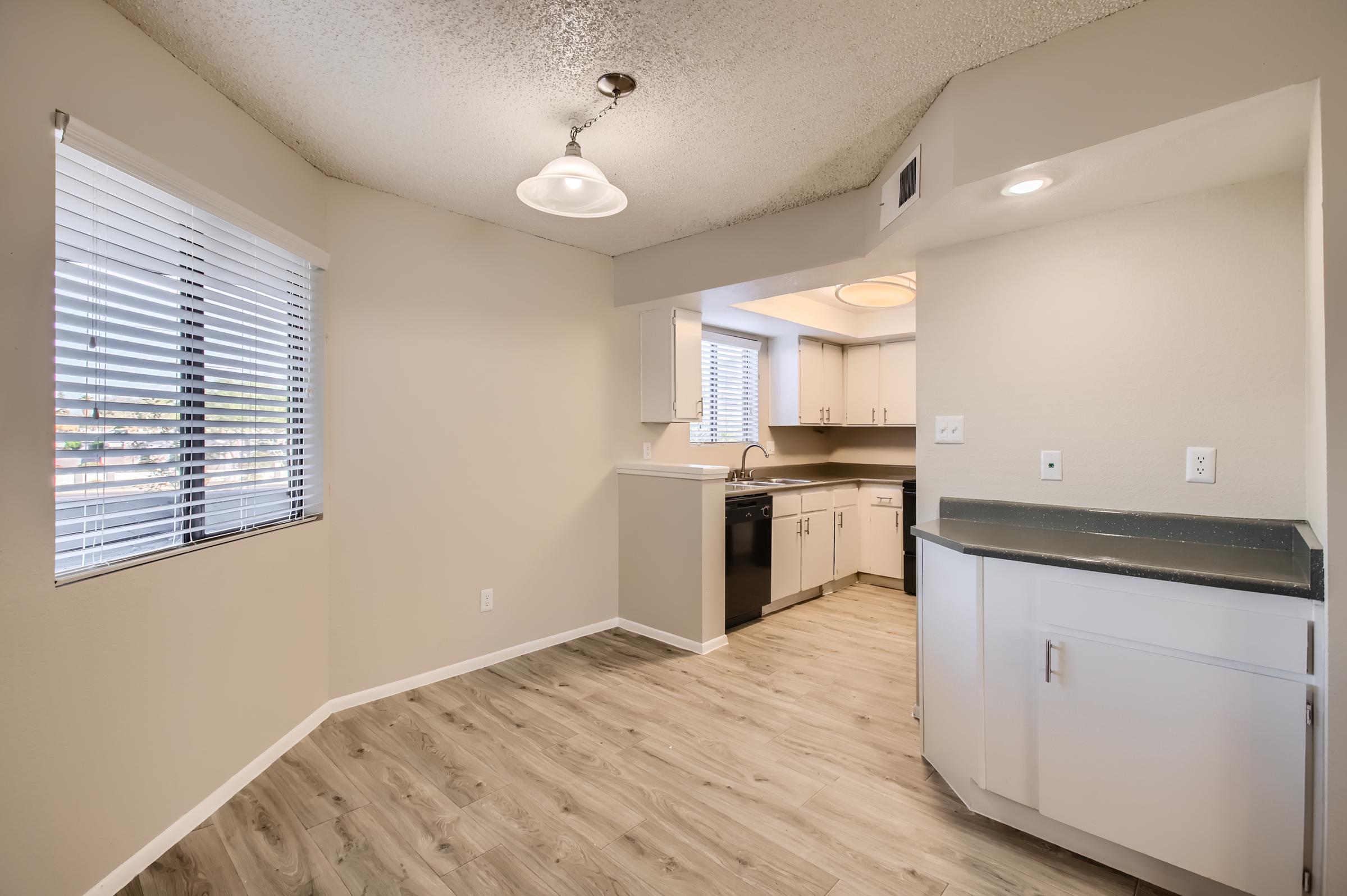 Rounded corner of a Phoenix, AZ apartment that turns toward a kitchen with white cabinets and black appliances