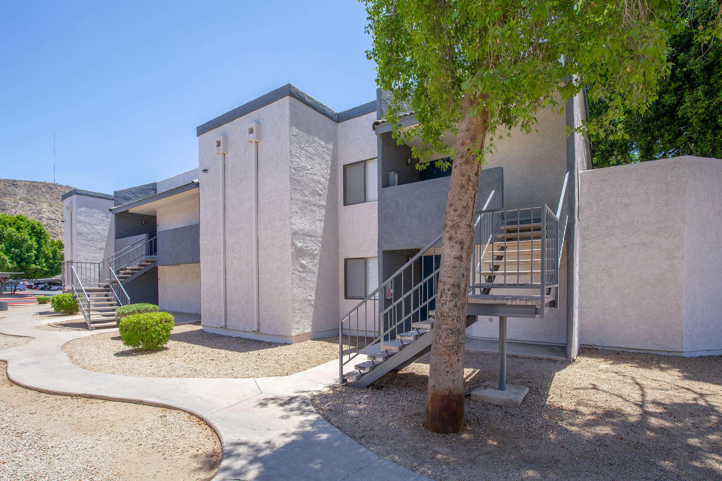 Outdoor view of a two-story Phoenix, AZ apartment building with landscaping and a tree at Rise Desert Cove
