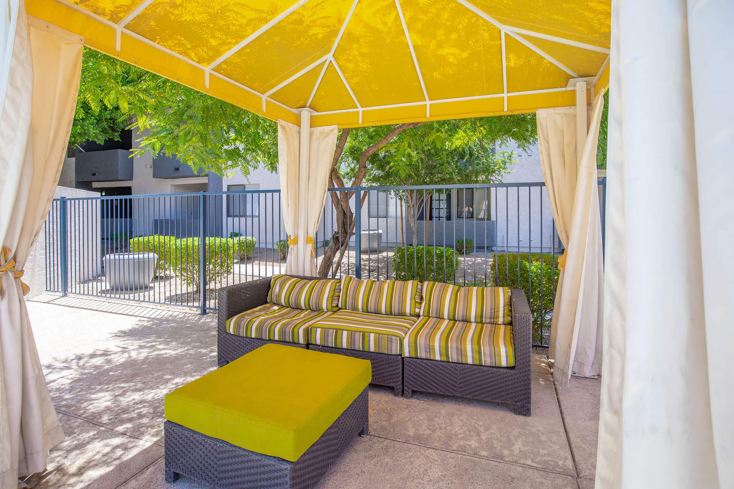 Outdoor yellow sofa and ottoman under a yellow fabric pool cabana at Rise Desert Cove