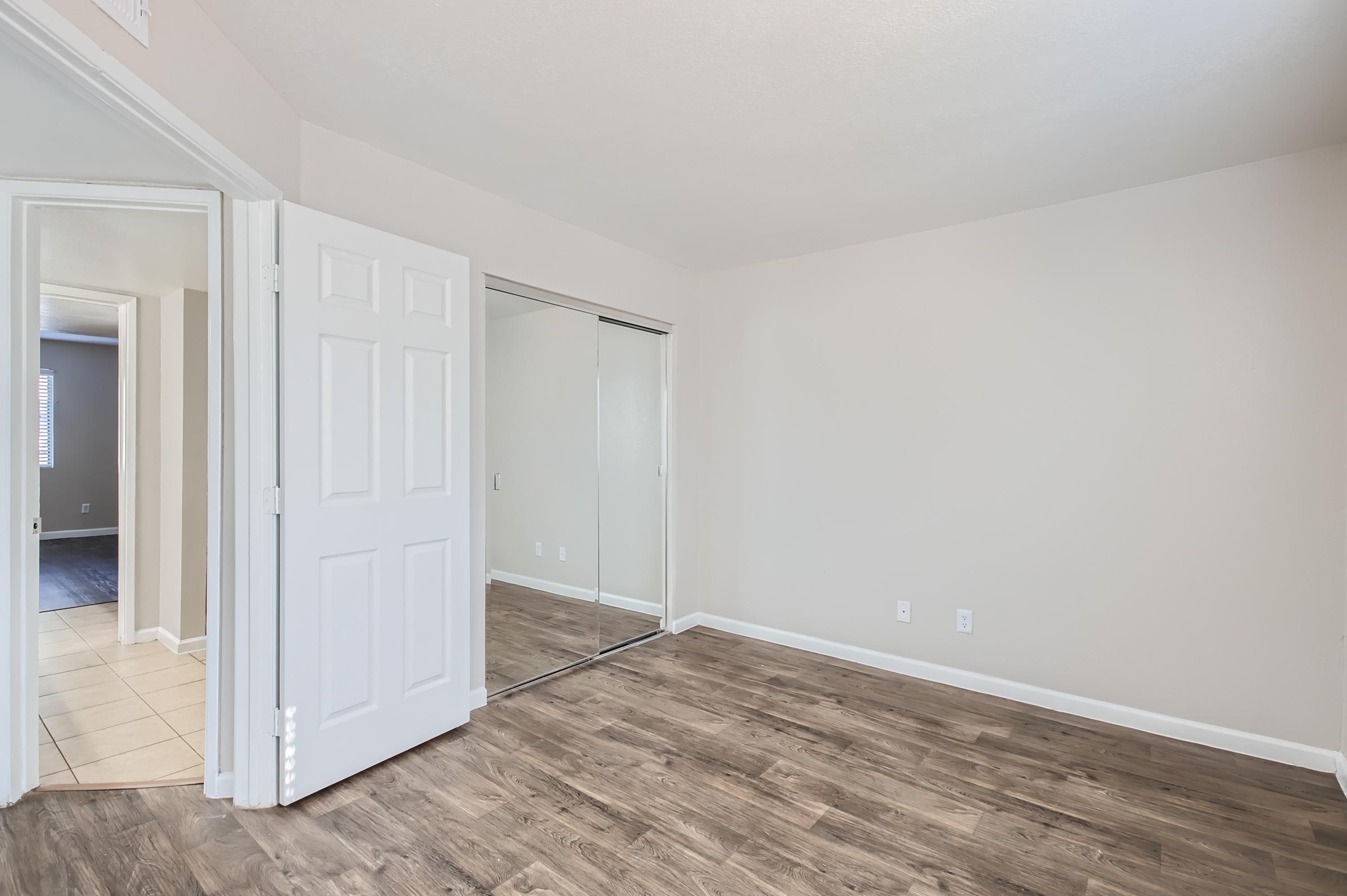 Empty Rise Desert Cove apartment bedroom with a wooden floor and door to the bathroom and mirrored closet sliding door to the left