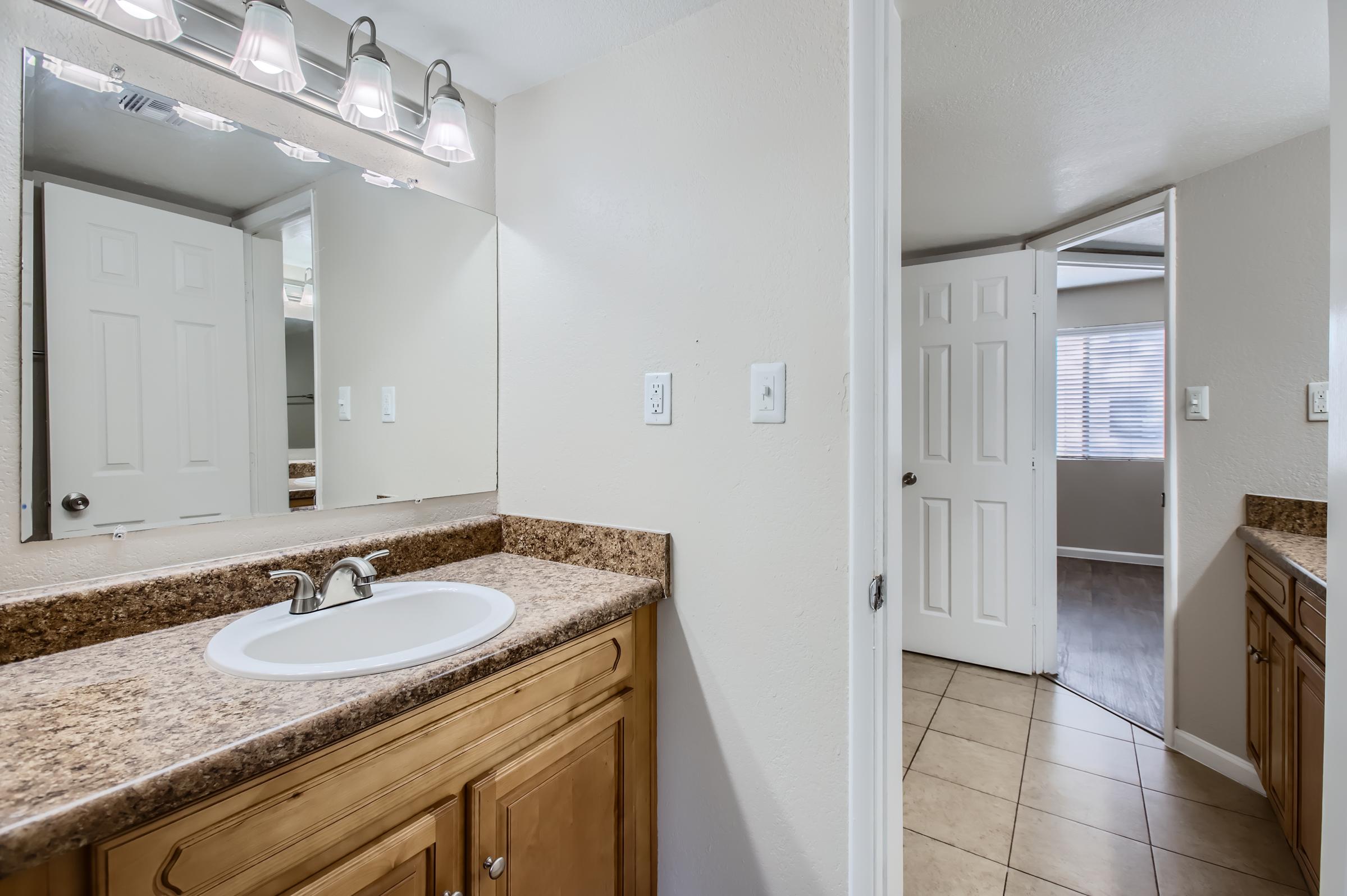 Rise Desert Cove apartment bathroom with a sink and mirror on the left and a view into another room in the front