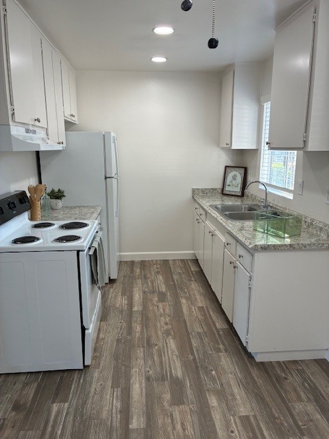 Bright and modern kitchen featuring white cabinetry, granite countertops, a double sink, and a white refrigerator. Appliances include an electric stove with four burners. The floor is made of light wood-like tiles, and there is a small window allowing natural light to enter. A decorative framed picture is placed on the counter.