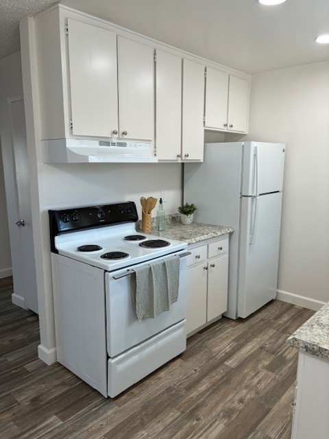 A clean, modern kitchen featuring white cabinets, a black stove with four burners, a white refrigerator, and a speckled countertop. The space is well-lit and includes wooden flooring. A few kitchen utensils are placed on the countertop for a welcoming touch.