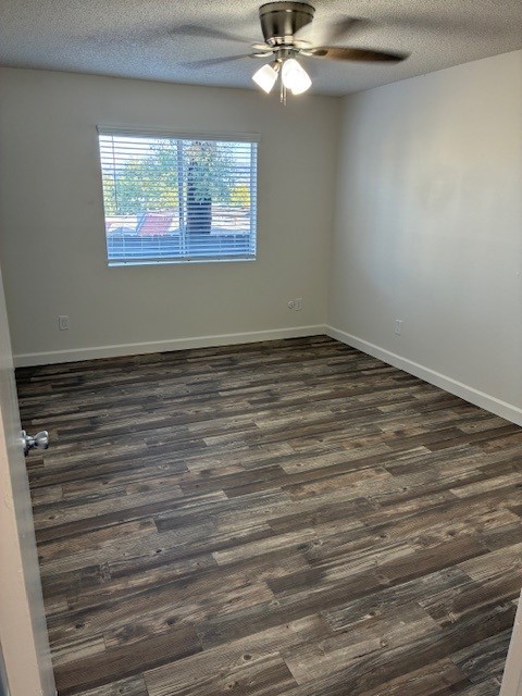 Empty room with light-colored walls and wooden flooring. A ceiling fan is mounted centrally, and a window with blinds lets in natural light. The space appears clean and well-maintained, suitable for various purposes such as a bedroom or office.