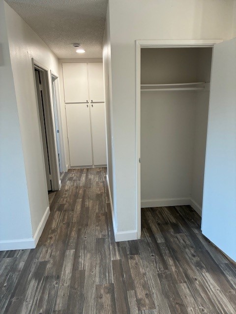 A well-lit hallway featuring light-colored walls and a wooden floor. On the left, there is a closed door leading to a room, and ahead, built-in closets with white doors. On the right, an open closet with no doors, showcasing a minimalist space. The overall atmosphere is clean and modern.