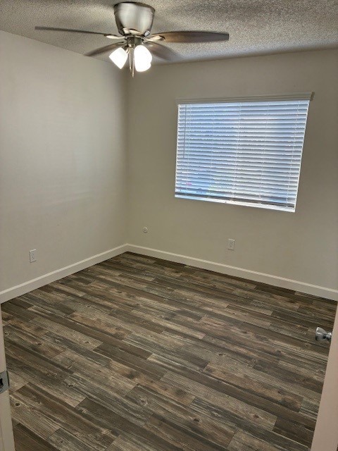 A small, empty room with light-colored walls and a window featuring blinds. The floor is covered in wooden-looking laminate. A ceiling fan with lights is installed, and the space feels bright and open, suitable for various furnishings.