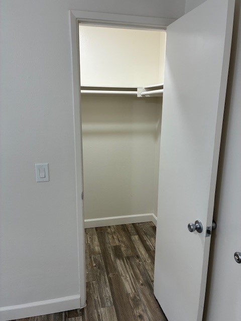 An empty closet with white walls and a hanging rod, wooden floor visible. The closet doors are open, revealing the spacious interior, which has no shelves or items inside. The overall color scheme is neutral, creating a clean and minimalistic appearance.