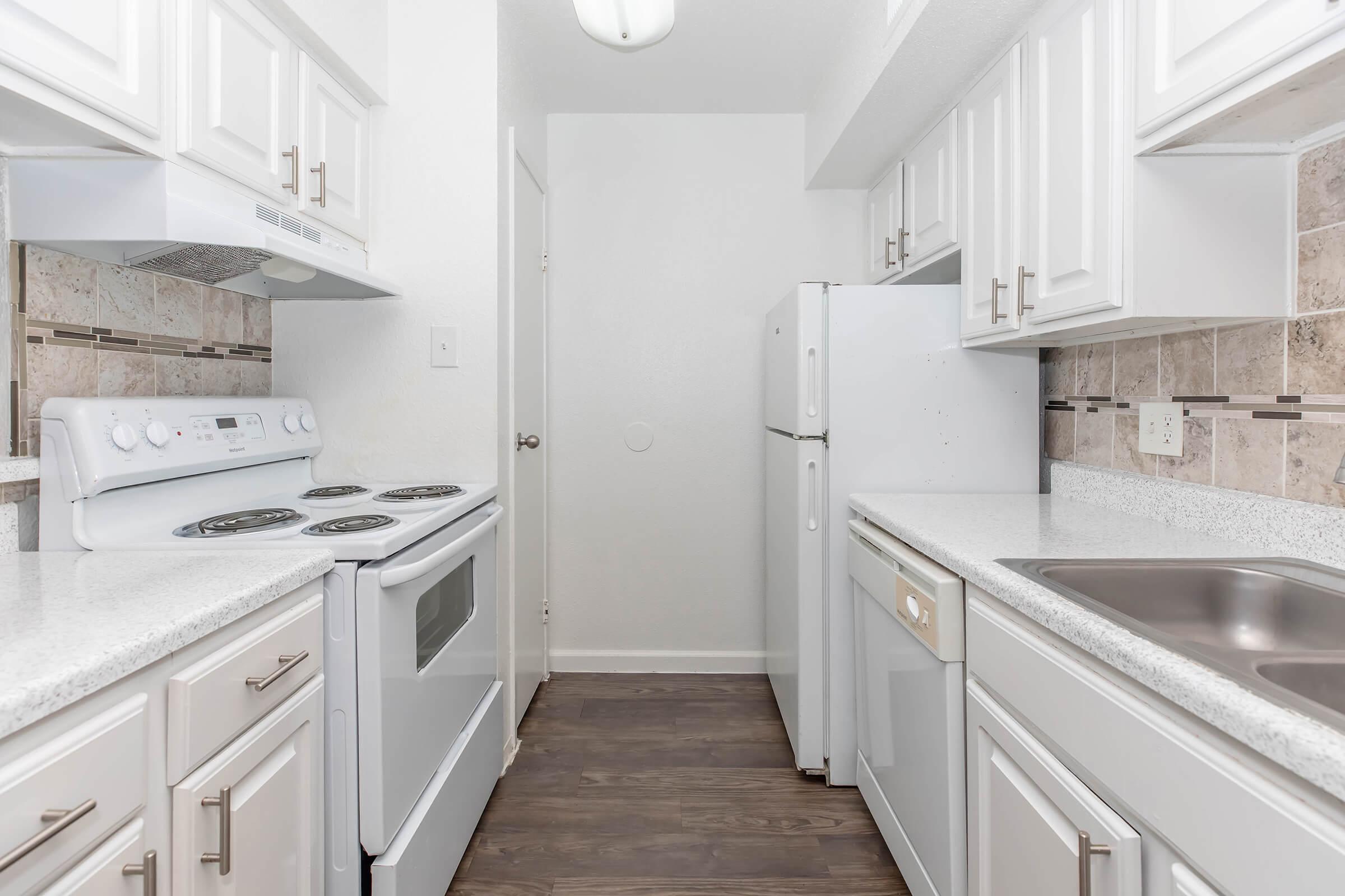 A modern kitchen featuring white cabinetry, stainless steel appliances, and light-colored countertops. The kitchen includes an electric stove, oven, refrigerator, and a sink, with tile backsplash and laminate flooring. Natural light illuminates the space, creating a clean and inviting atmosphere.