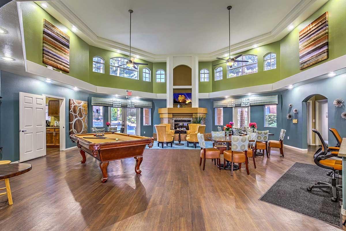 A spacious and elegantly designed room featuring a billiard table, dining area, and comfortable seating. Large windows allow natural light to fill the space, which is decorated in calming colors. A fireplace adds warmth, and modern furnishings create a welcoming atmosphere ideal for relaxation and social gatherings.