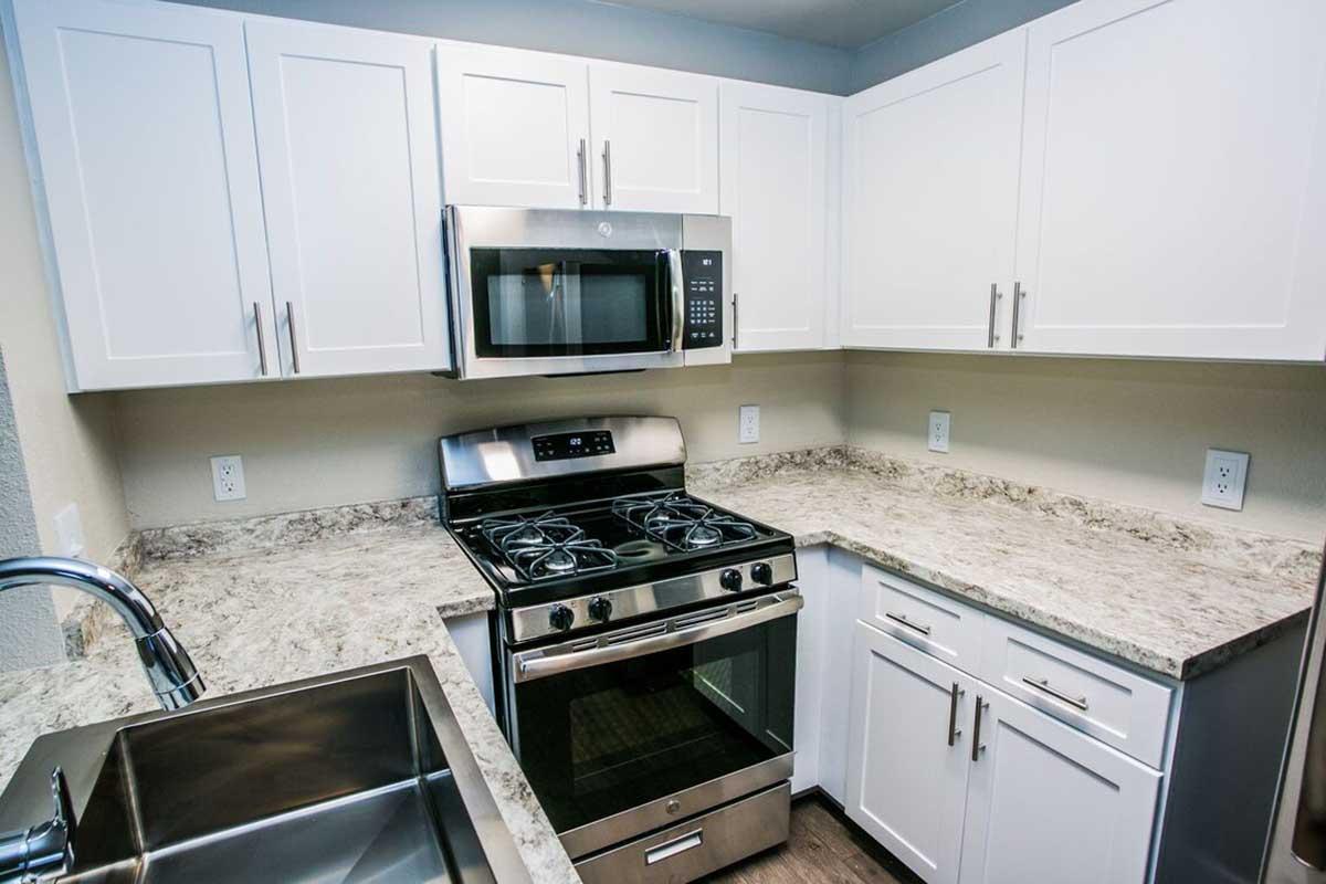 Modern kitchen featuring white cabinets, a stainless steel gas stove, a microwave above it, and granite countertops. The sink is visible, positioned near the corner, creating a stylish and functional cooking space.