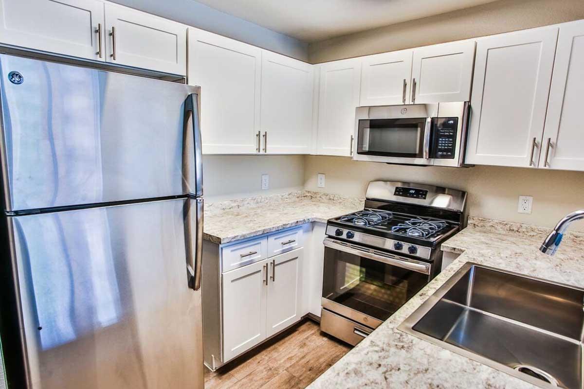 A modern kitchen featuring stainless steel appliances, including a refrigerator, stove, and microwave. The cabinets are white with sleek handles, and the countertop is a light-colored granite. A stainless steel sink is integrated into the countertop, enhancing the kitchen's contemporary design.