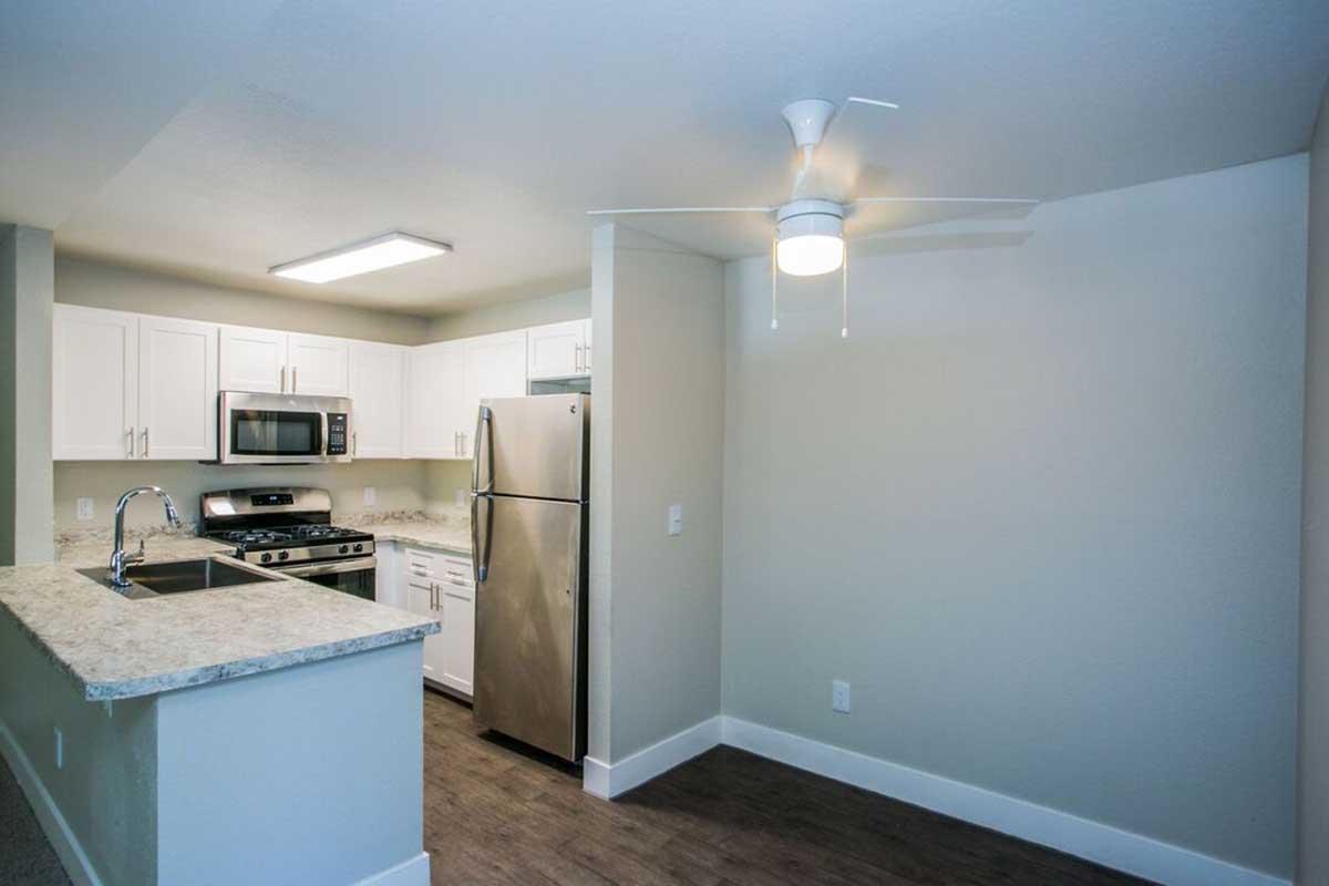Modern kitchen featuring white cabinets, stainless steel appliances, and a granite countertop island. Includes a ceiling fan and an open layout connecting to the living area. The space is well-lit with natural light and a large window, creating a bright and inviting atmosphere.