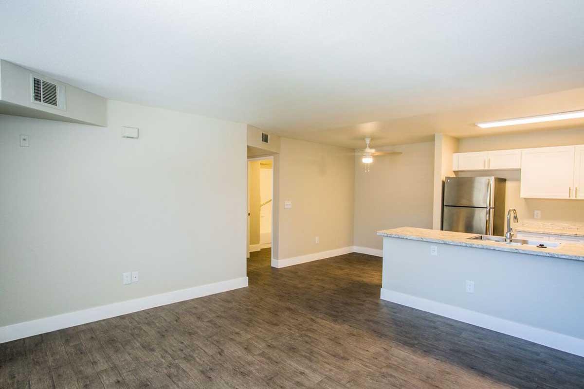 Spacious, modern apartment interior featuring an open floor plan. Includes a kitchen with stainless steel appliances, granite countertops, and a ceiling fan. Neutral-colored walls and flooring provide a bright and inviting atmosphere, with doorways leading to additional rooms.