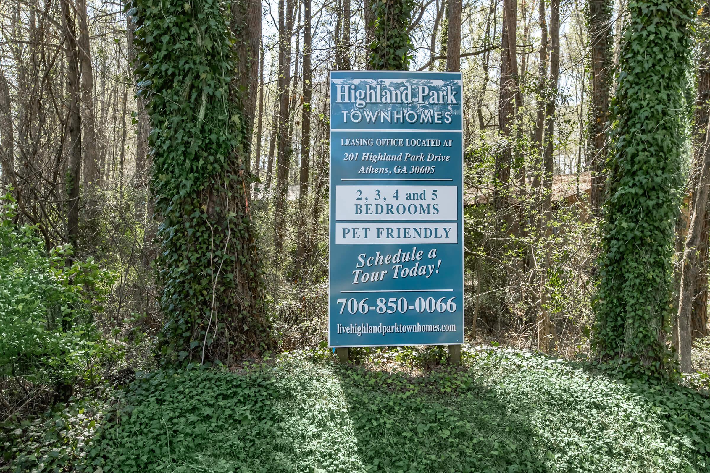 A sign for Highland Park Townhomes, displaying leasing information. It mentions the office location at 201 Highland Park Drive, Athens, GA 30605, and offers 2, 3, 4, and 5-bedroom options. The sign also highlights that it is pet-friendly and includes a phone number to schedule a tour.