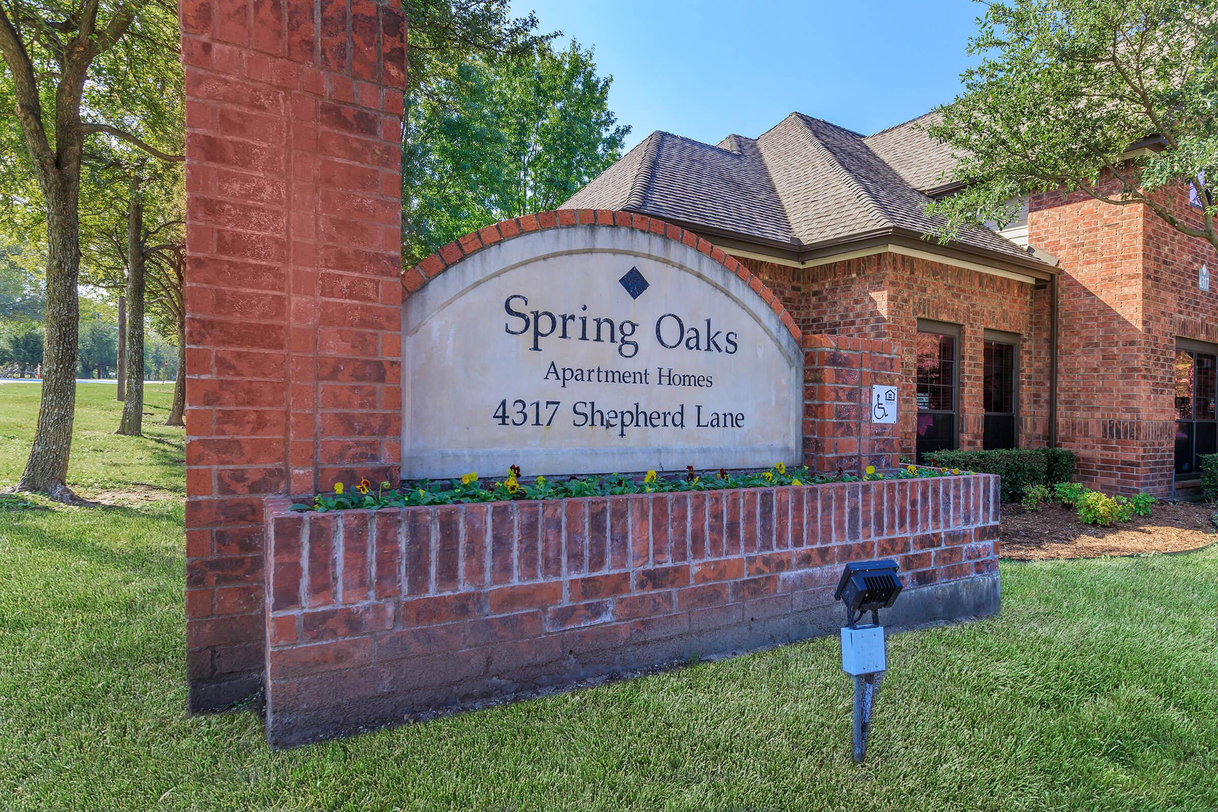 Sign for Spring Oaks Apartment Homes located at 4317 Shepherd Lane. The sign features brick masonry and greenery surrounding it, with the name and address clearly displayed.