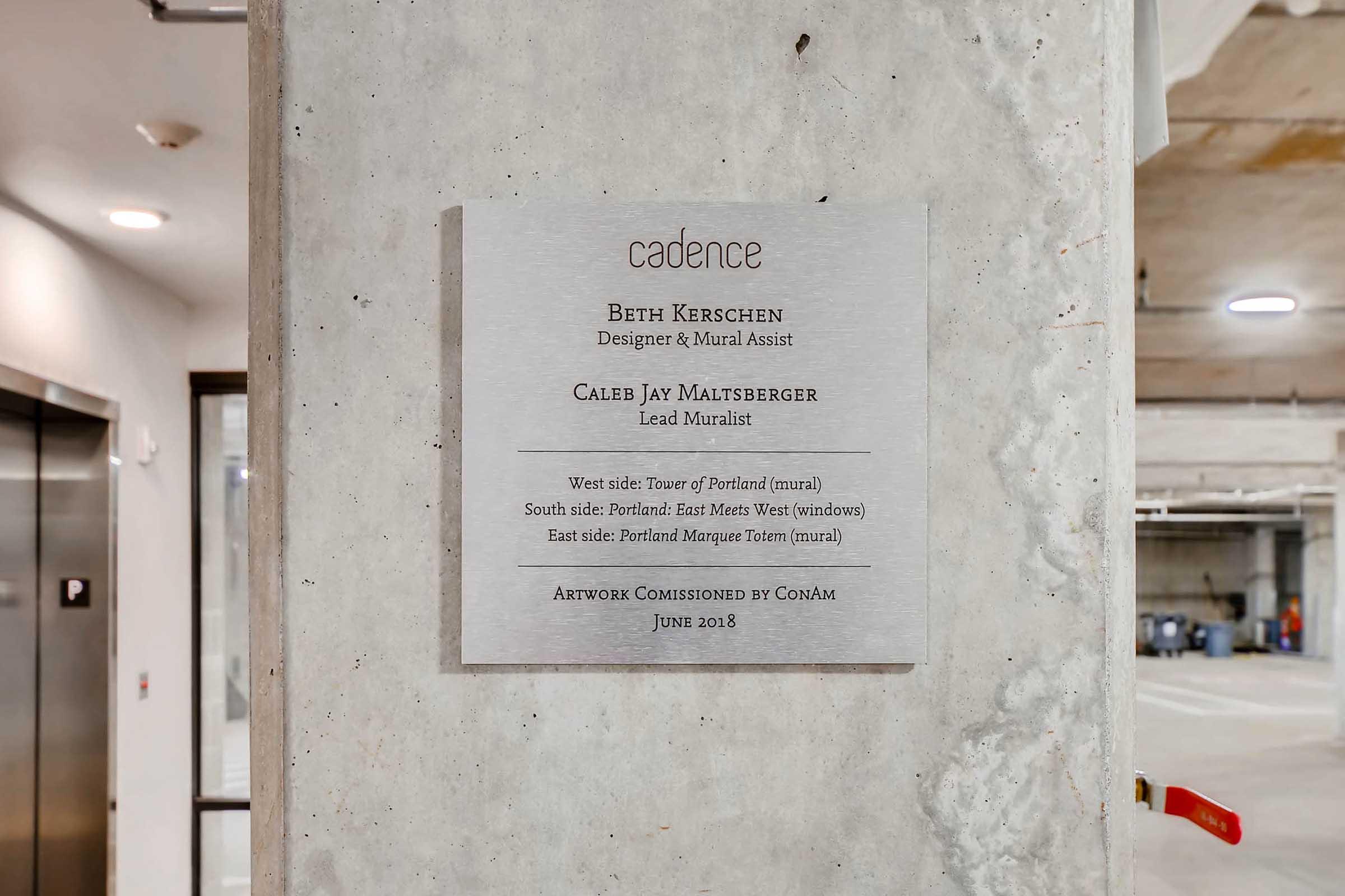 Signage mounted on a concrete wall, detailing information about a mural project by artists