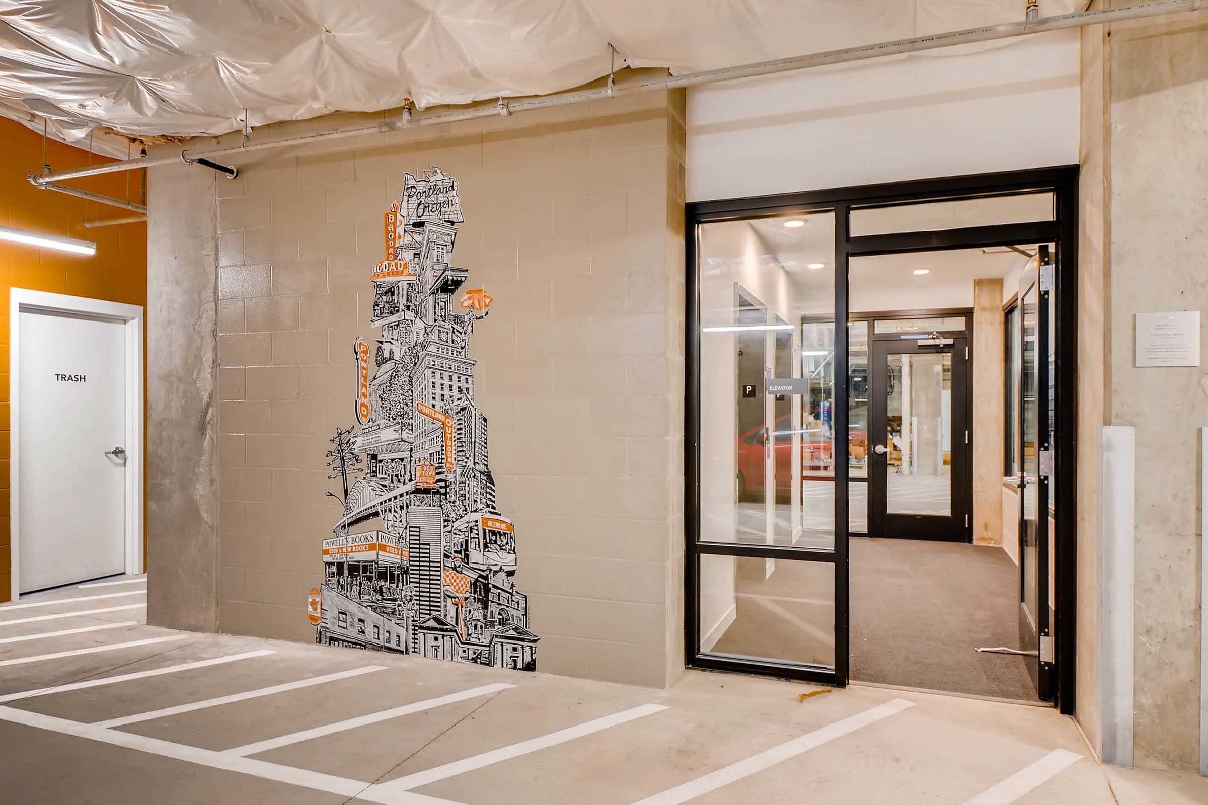 A mural featuring a tall, stylized building design in black and orange is displayed on a gray wall.