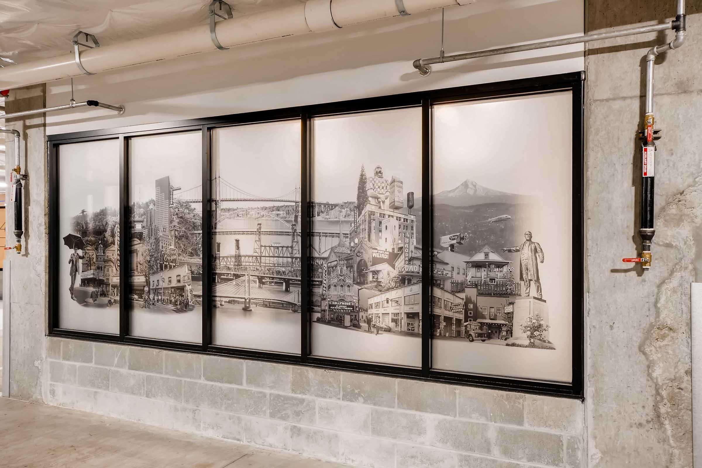 A large, black-framed mural featuring a collage of historic images from various locations, including bridges, buildings, and landmarks, displayed on a wall in an industrial setting. The images have a vintage aesthetic, blending together to create a cohesive look.