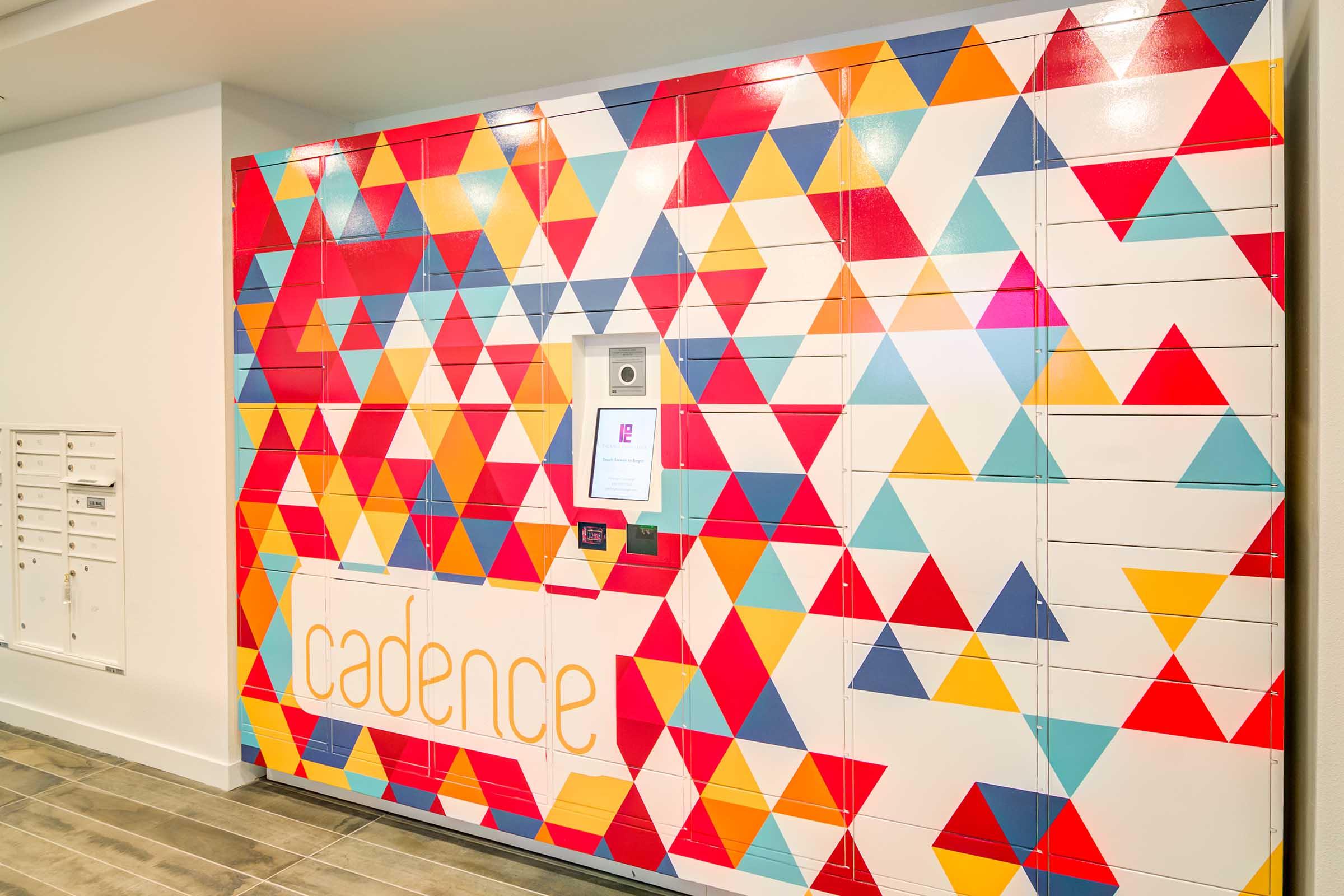 Colorful wall design featuring a vibrant pattern of red, blue, yellow, and white triangles. A digital interface is centered among the triangles, with the word "cadence" displayed prominently in a modern font. The surrounding area includes mailboxes on the left side.
