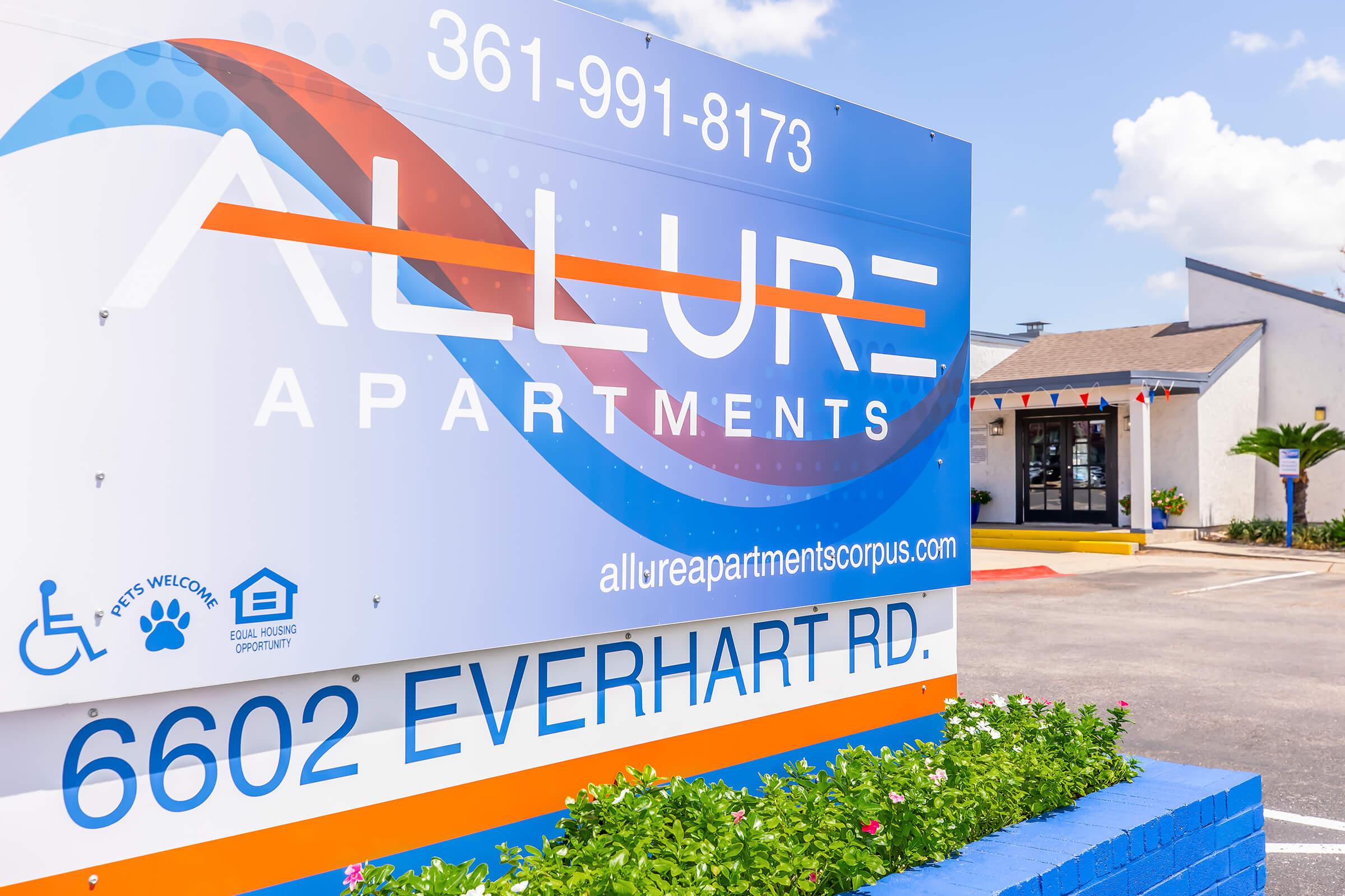 Sign for Allure Apartments located at 6602 Everhart Rd, featuring contact number 361-991-8173. The sign includes symbols indicating accessibility, pet-friendly policies, and a website URL for more information. Colorful design elements create a welcoming appearance.