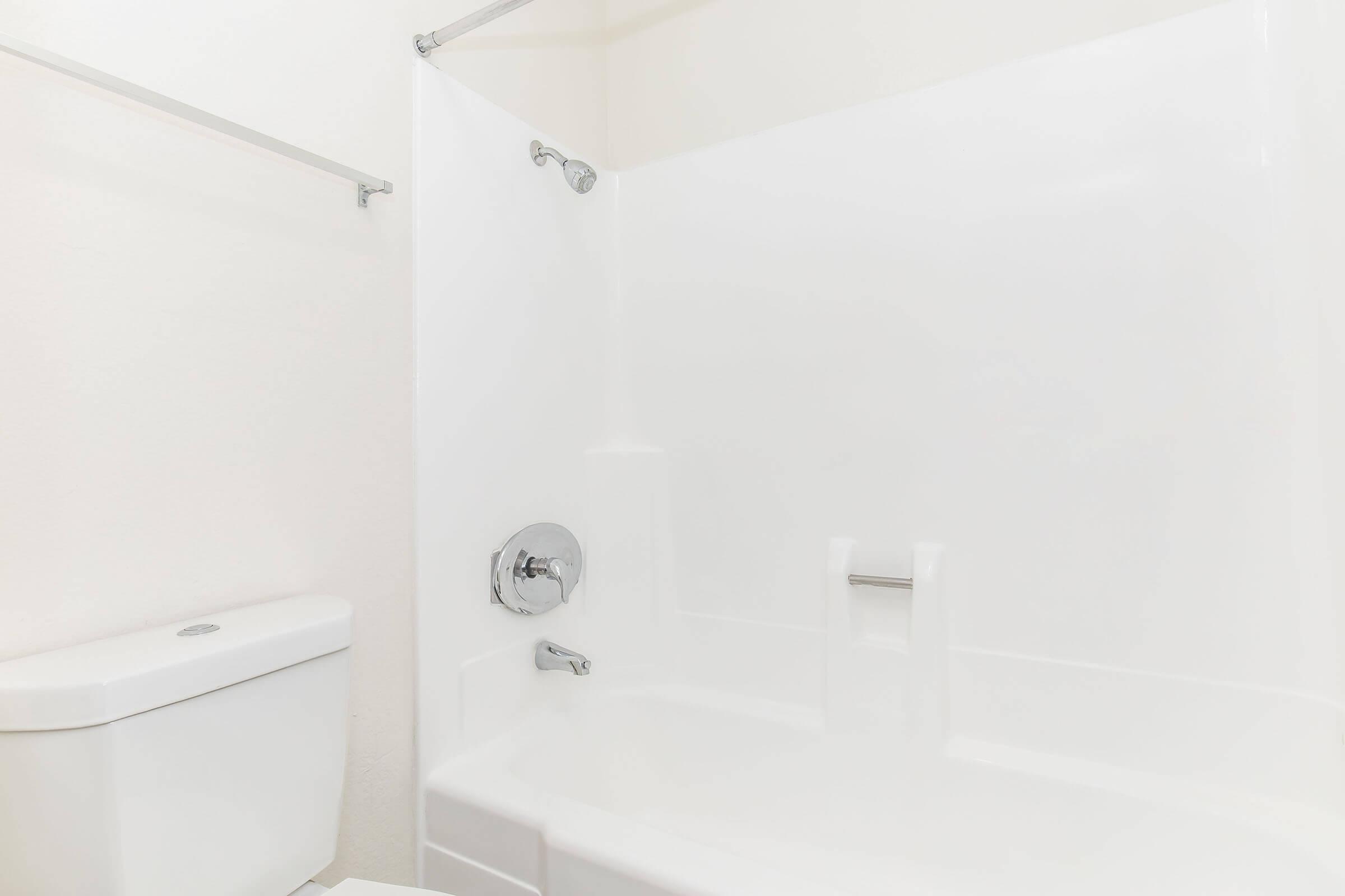 A clean, white bathroom featuring a bathtub with a showerhead, a single faucet, and a modern toilet. The walls and fixtures are minimalist with a bright, airy feel. The overall aesthetic is simple and uncluttered, emphasizing a fresh and inviting atmosphere.