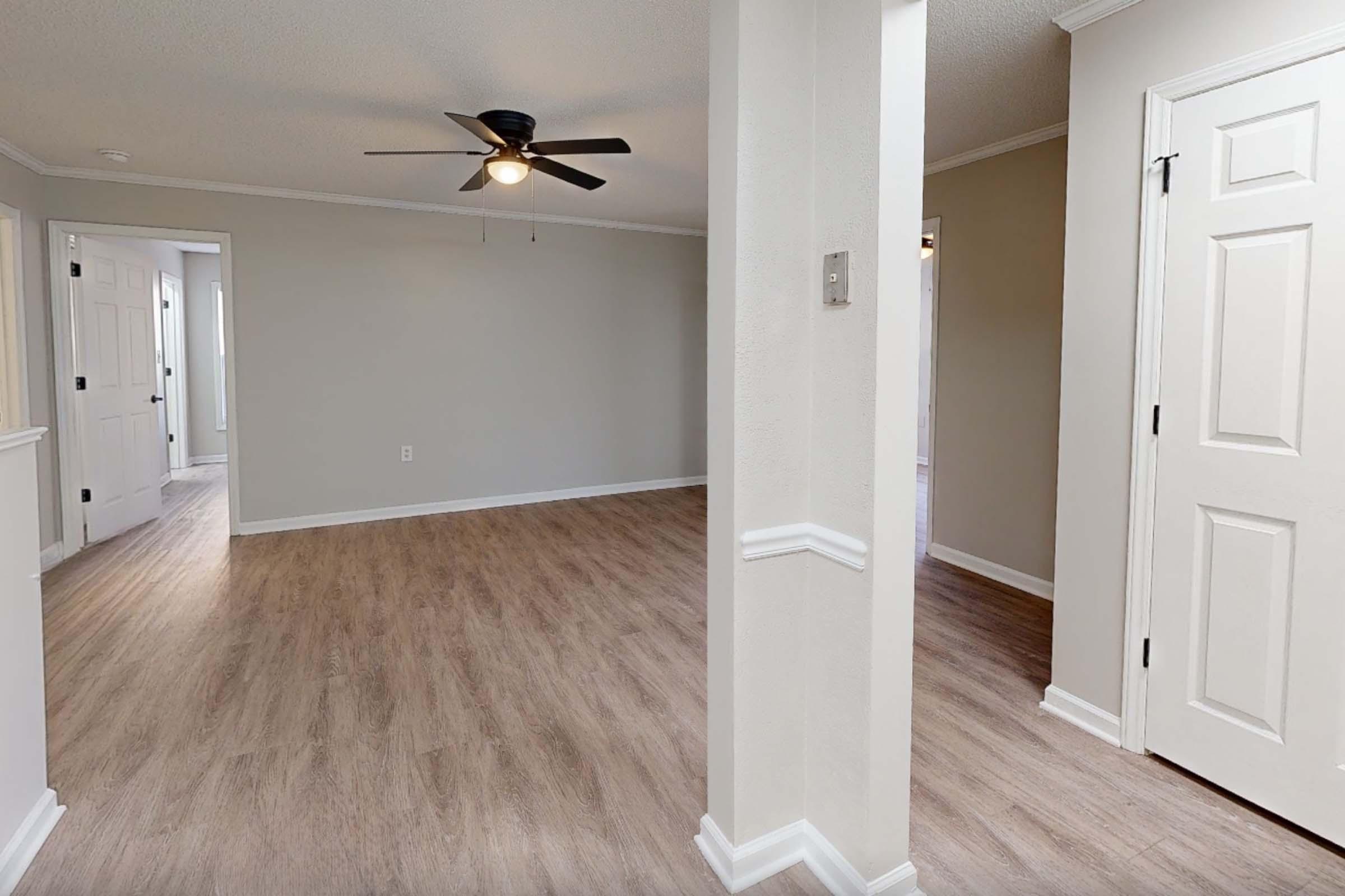 A spacious, well-lit room with light-colored walls and hardwood flooring. A ceiling fan is installed, and there are doorways leading to other areas. A decorative molding runs along the walls, adding elegance to the space. The overall atmosphere is inviting and modern.