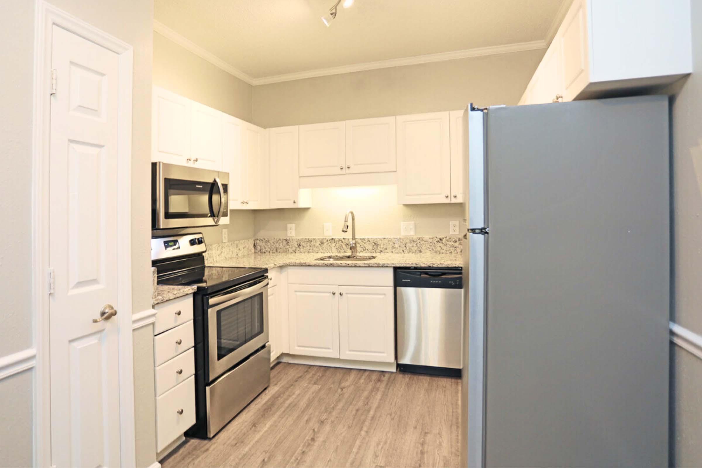 Modern kitchen featuring white cabinets, stainless steel appliances including a microwave, oven, and dishwasher, granite countertops, and a light hardwood floor. The kitchen has a clean, spacious design with under-cabinet lighting and neutral wall color, creating a bright and inviting atmosphere.