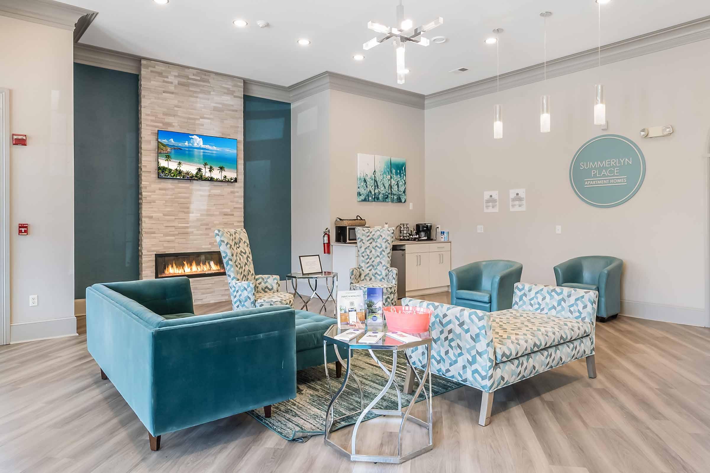 A modern waiting area featuring comfortable teal chairs and a light-colored sofa. There’s a decorative stone wall with a fireplace, a table displaying brochures, and a serene coastal-themed artwork on the wall. Soft lighting and neutral colors create a welcoming atmosphere.