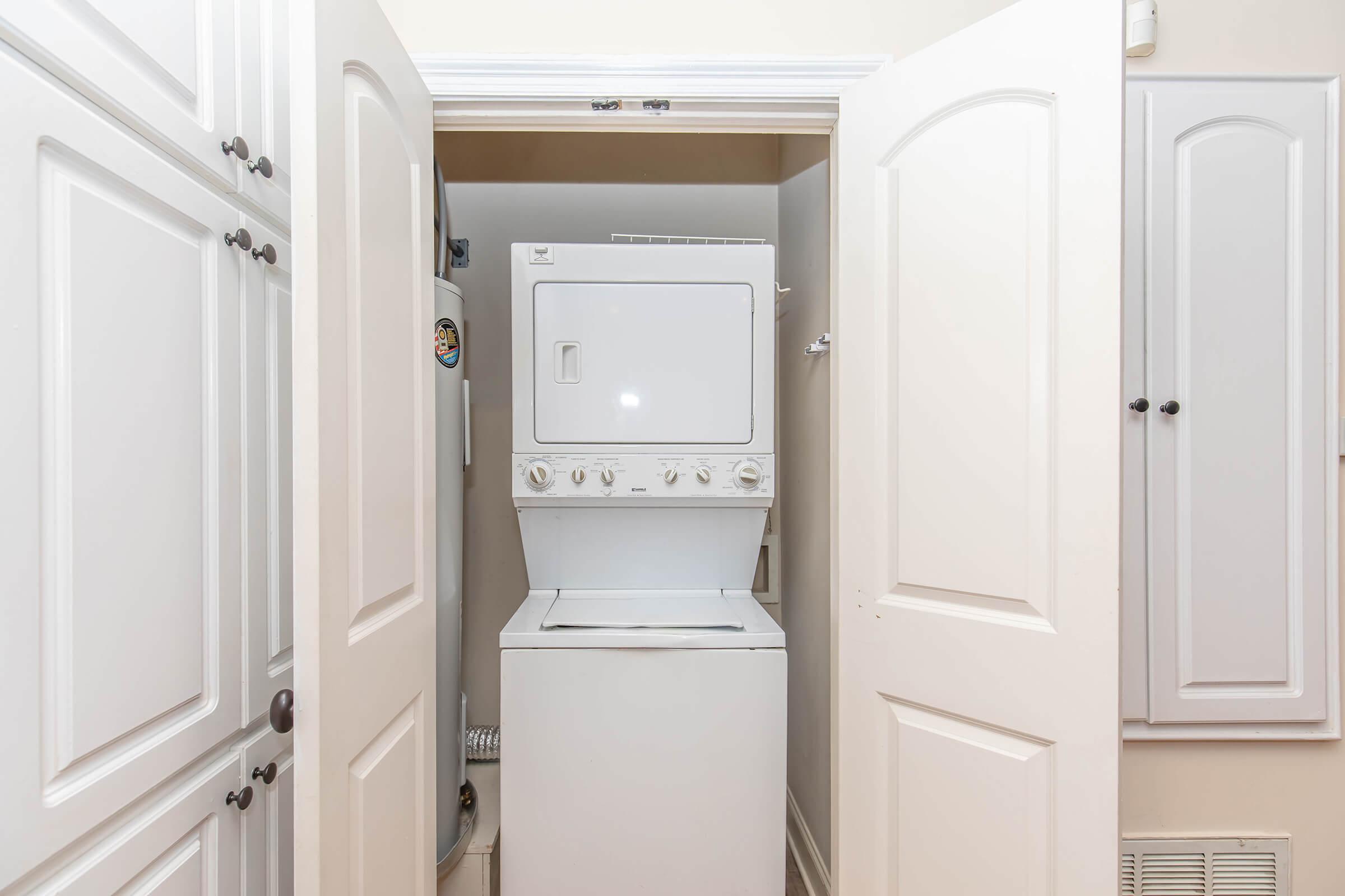 A compact laundry area featuring a stacked washer and dryer unit, positioned between two closed cabinet doors. The walls are painted a light color, and there are additional cabinet storage options nearby. The space is designed for efficient use in a small area.
