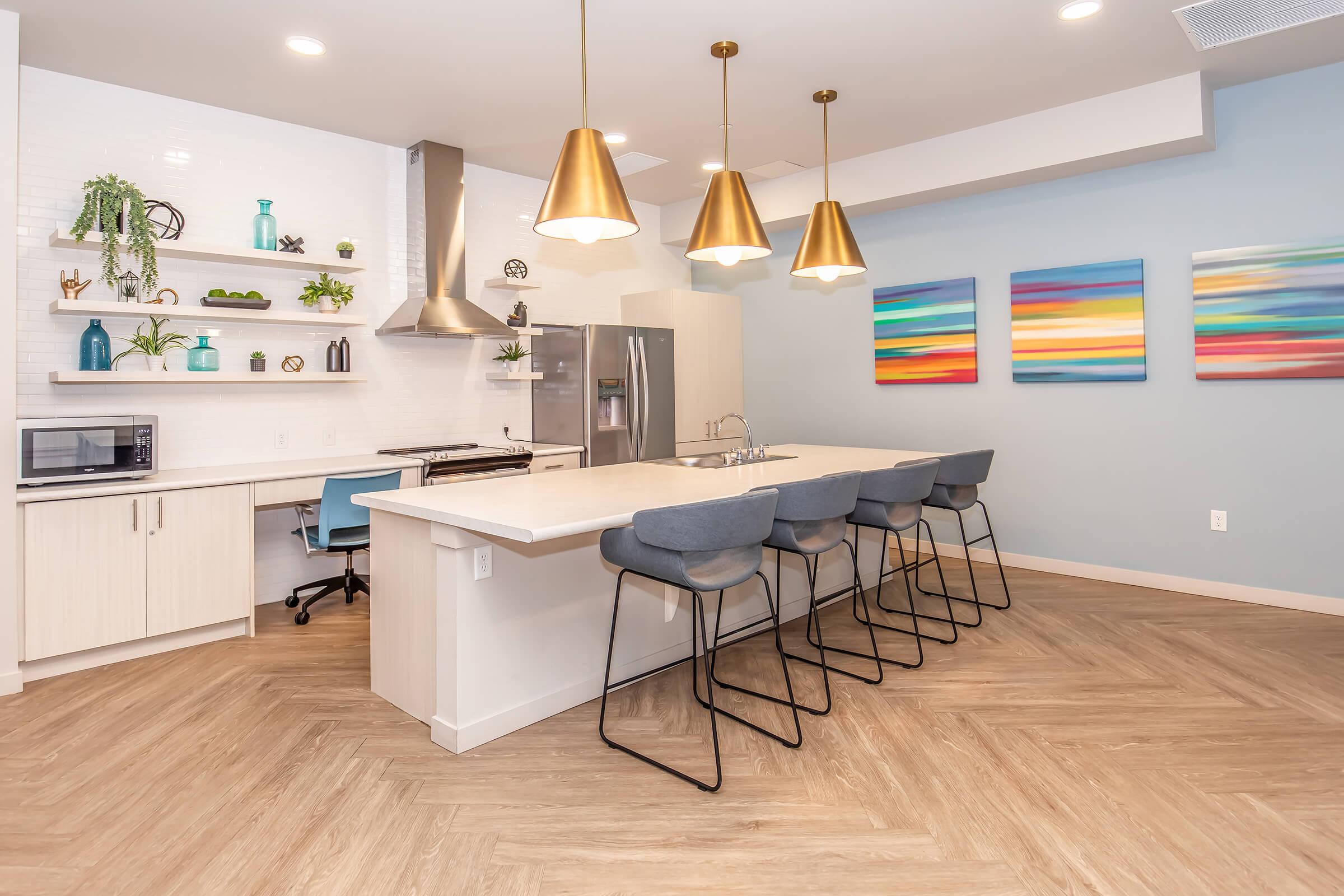 Modern kitchen featuring a large island with four high-backed stools, sleek cabinetry, and stainless-steel appliances. A stylish range hood is above the stove, and open shelving displays decorative plants and items. Colorful abstract artwork hangs on the wall, complementing the contemporary decor.