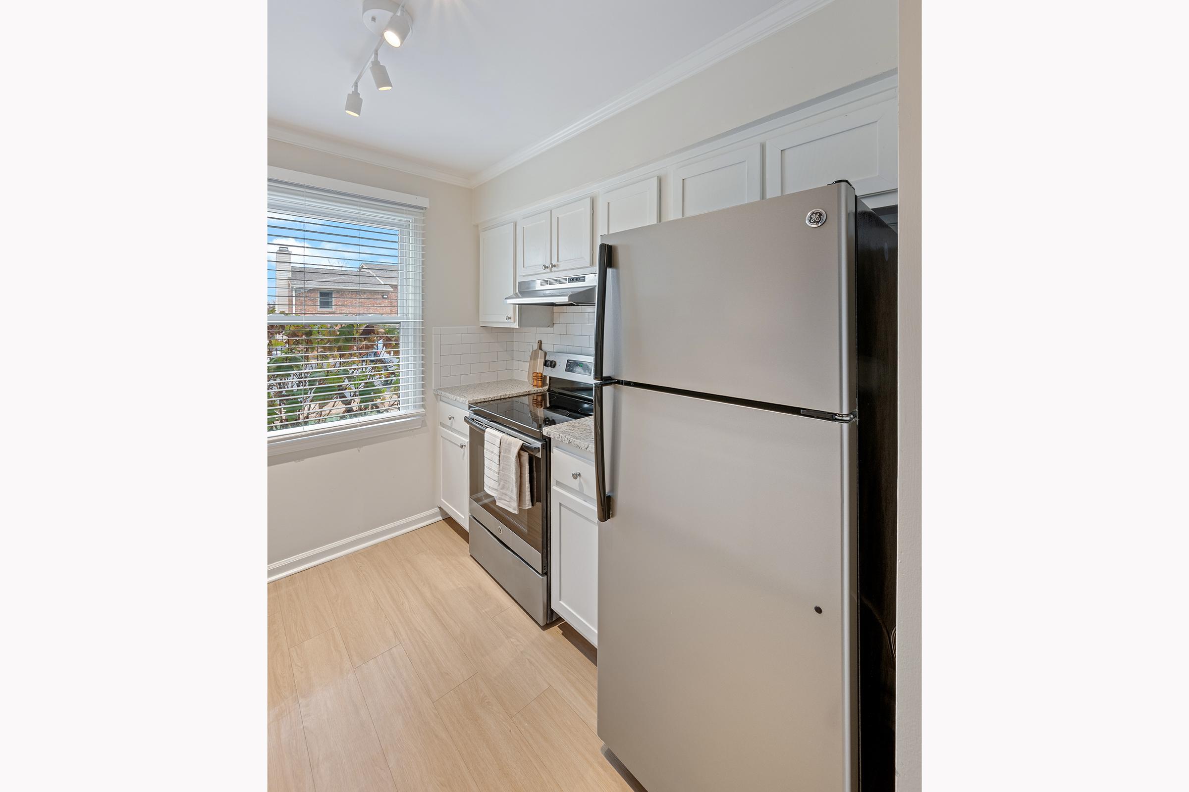 Modern kitchen featuring stainless steel appliances including a refrigerator, stove, and dishwasher. White cabinets with a light countertop, and a window providing natural light. The floor is light-colored, enhancing the bright and airy feel of the space.