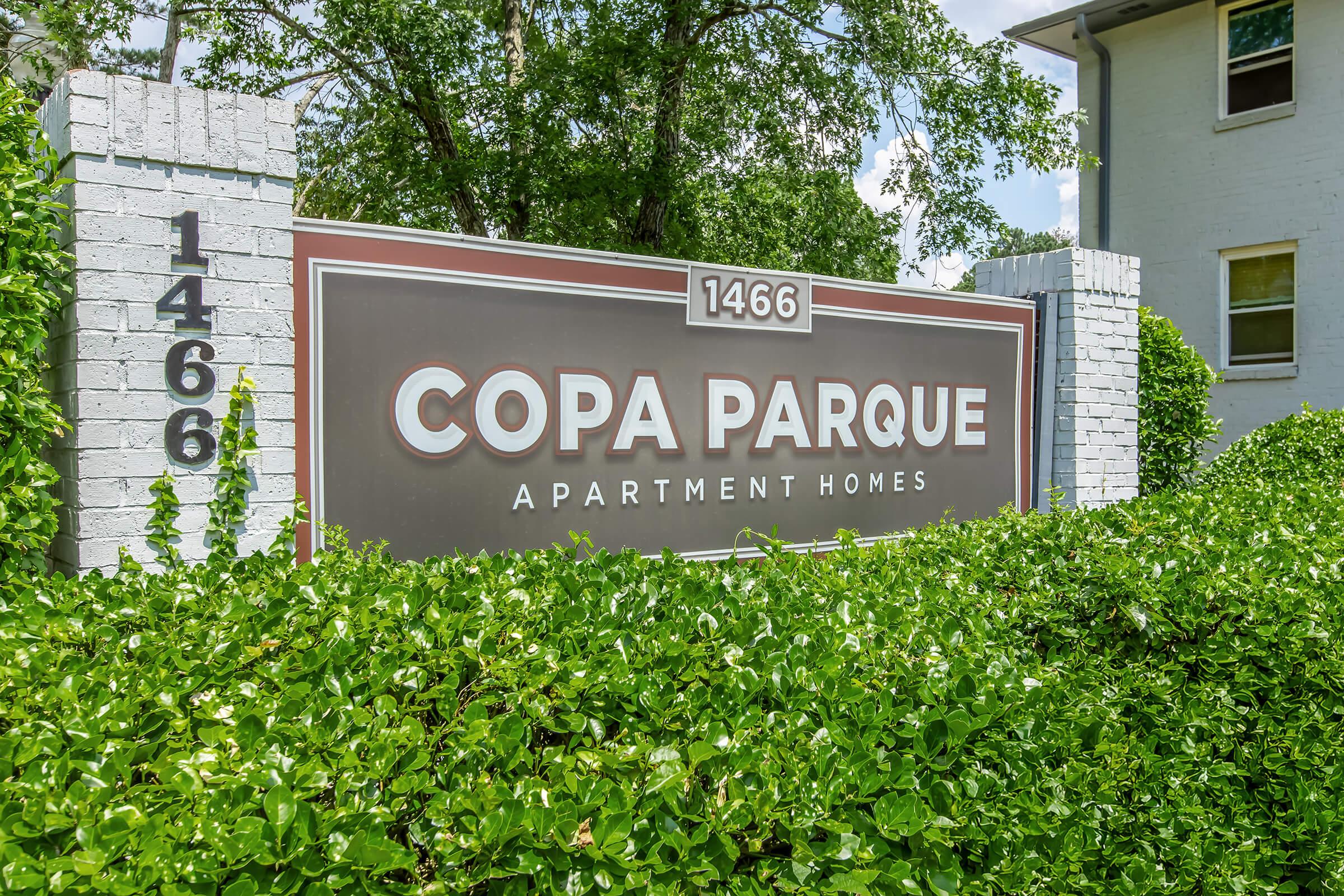 Sign for Copa Parque Apartment Homes with the address 1466, partially obscured by green shrubs. The sign is displayed prominently, indicating a residential complex.