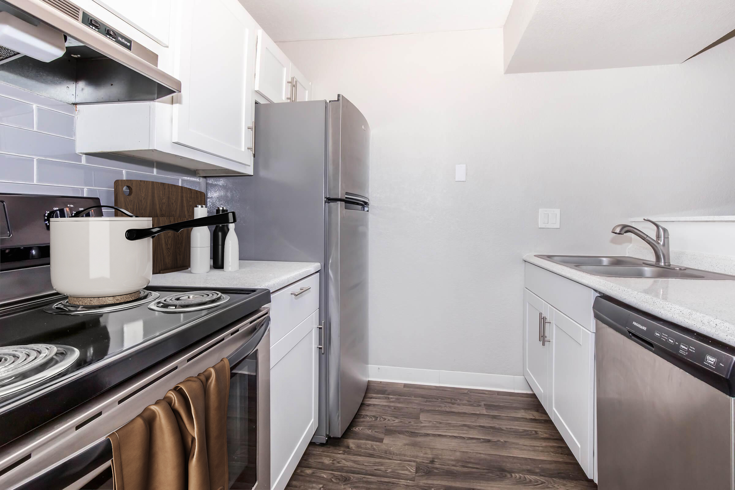 A modern kitchen featuring white cabinetry, stainless steel appliances, and gray tile backsplash. The stove has a pot on it, and there is a stainless steel refrigerator, a sink, and a dishwasher. The countertop is light-colored, and the flooring is a wood-like laminate.