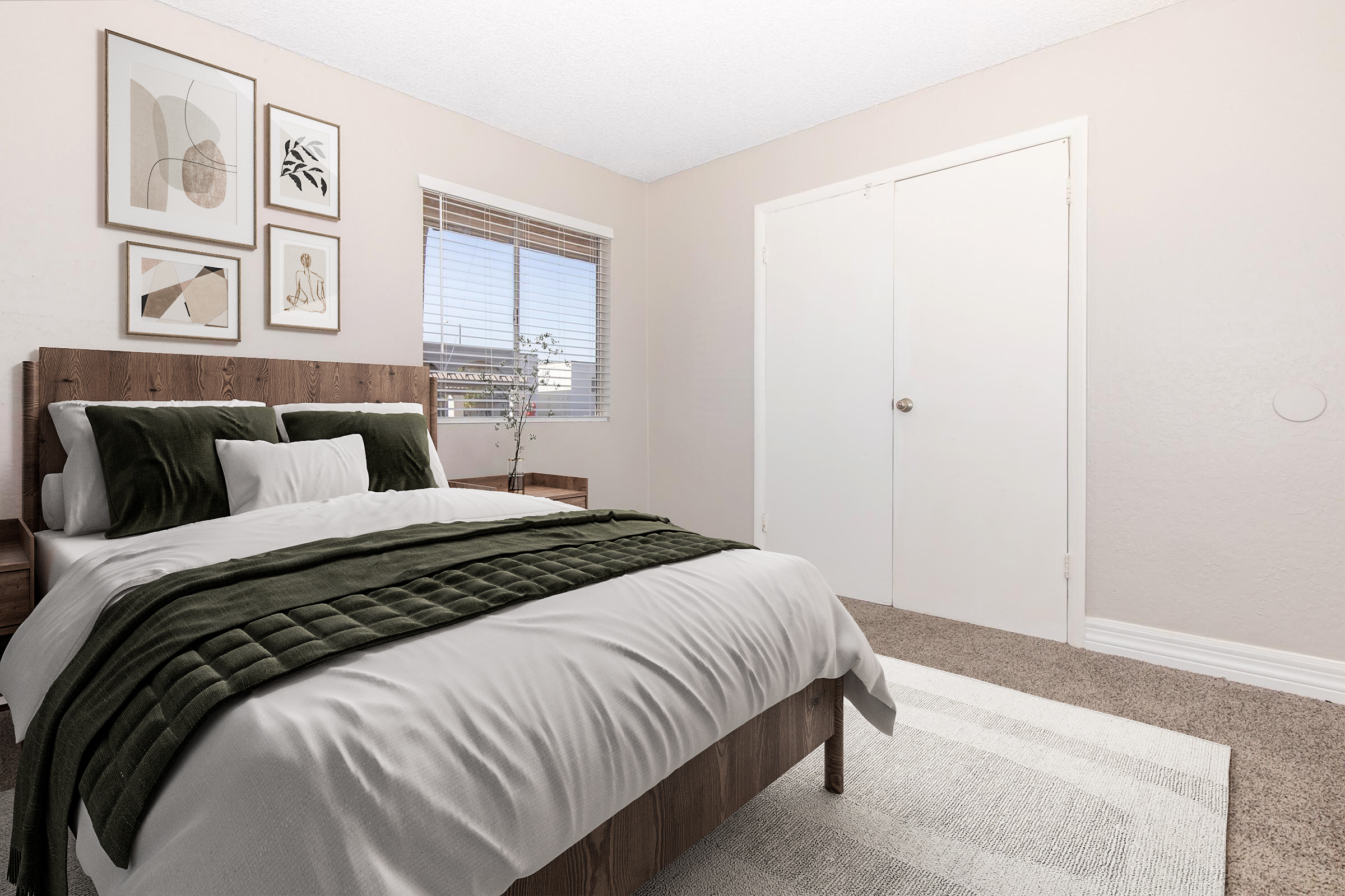 A cozy bedroom featuring a wooden bed with an olive green blanket, white pillows, and a nightstand. The room has light-colored walls, a rug, and a window with modern art frames on the wall. A closed white door is visible, complementing the neutral color palette.