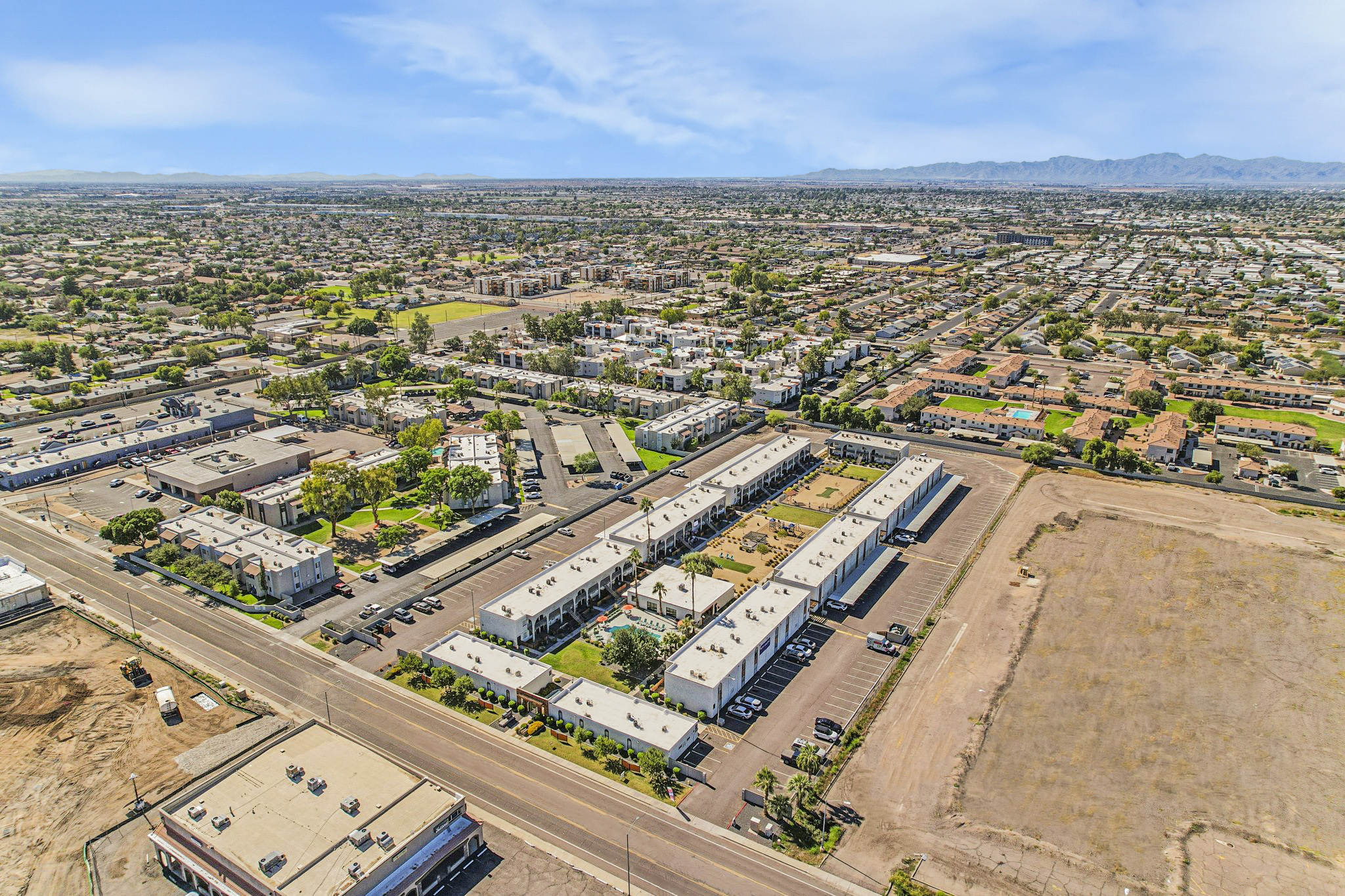 An aerial view of a suburban area featuring a mix of residential buildings and commercial properties. The landscape includes parking lots, green spaces, and nearby mountains in the background. Roads and neighborhoods are visible, showcasing a blend of developed and undeveloped land.