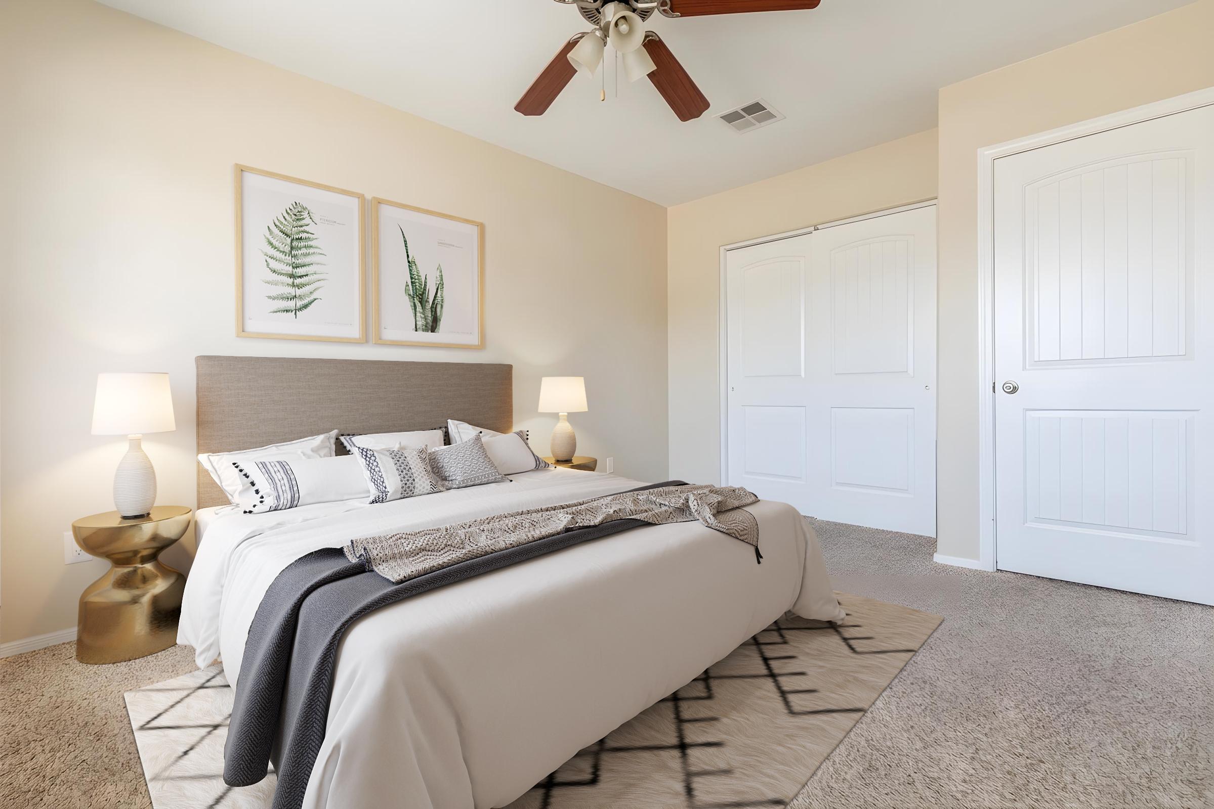 A neatly arranged bedroom featuring a beige wall, a king-sized bed with decorative pillows and a throw blanket, two bedside lamps, and artwork of plants. There is a light-colored rug on the carpeted floor, a door leading to a closet, and natural light illuminating the space.