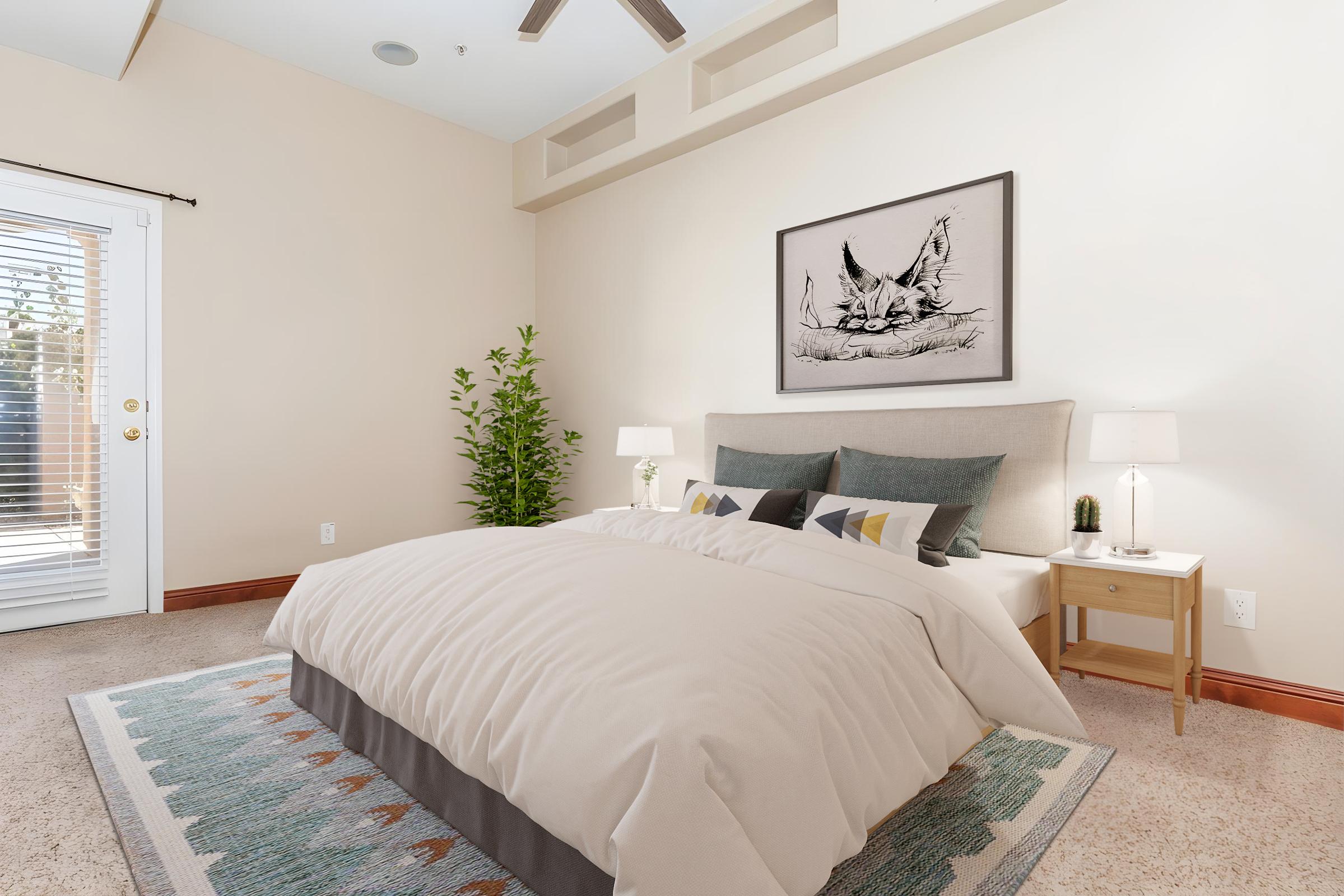 A cozy bedroom featuring a queen-sized bed with a light-colored comforter and decorative pillows. There is a framed artwork above the bed, bedside tables with lamps, and a small plant. A window with blinds allows natural light to enter, creating a warm and inviting atmosphere.