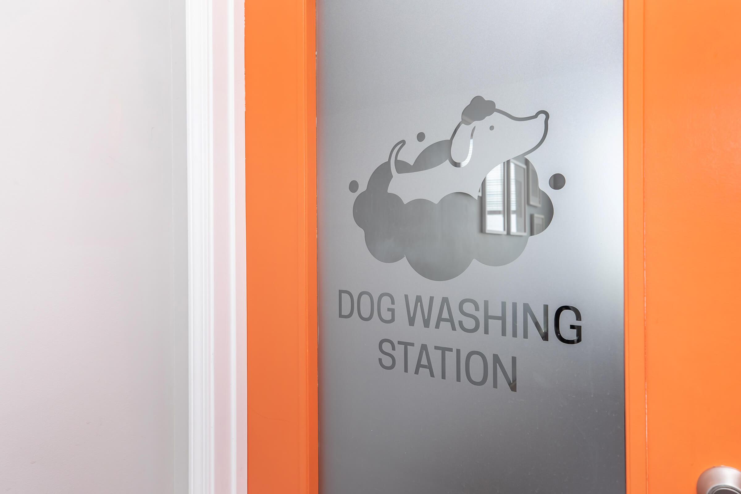 Frosted glass door featuring a playful dog illustration above the text "DOG WASHING STATION." The door is framed in bright orange, adding a vibrant touch to the space designed for pet grooming.