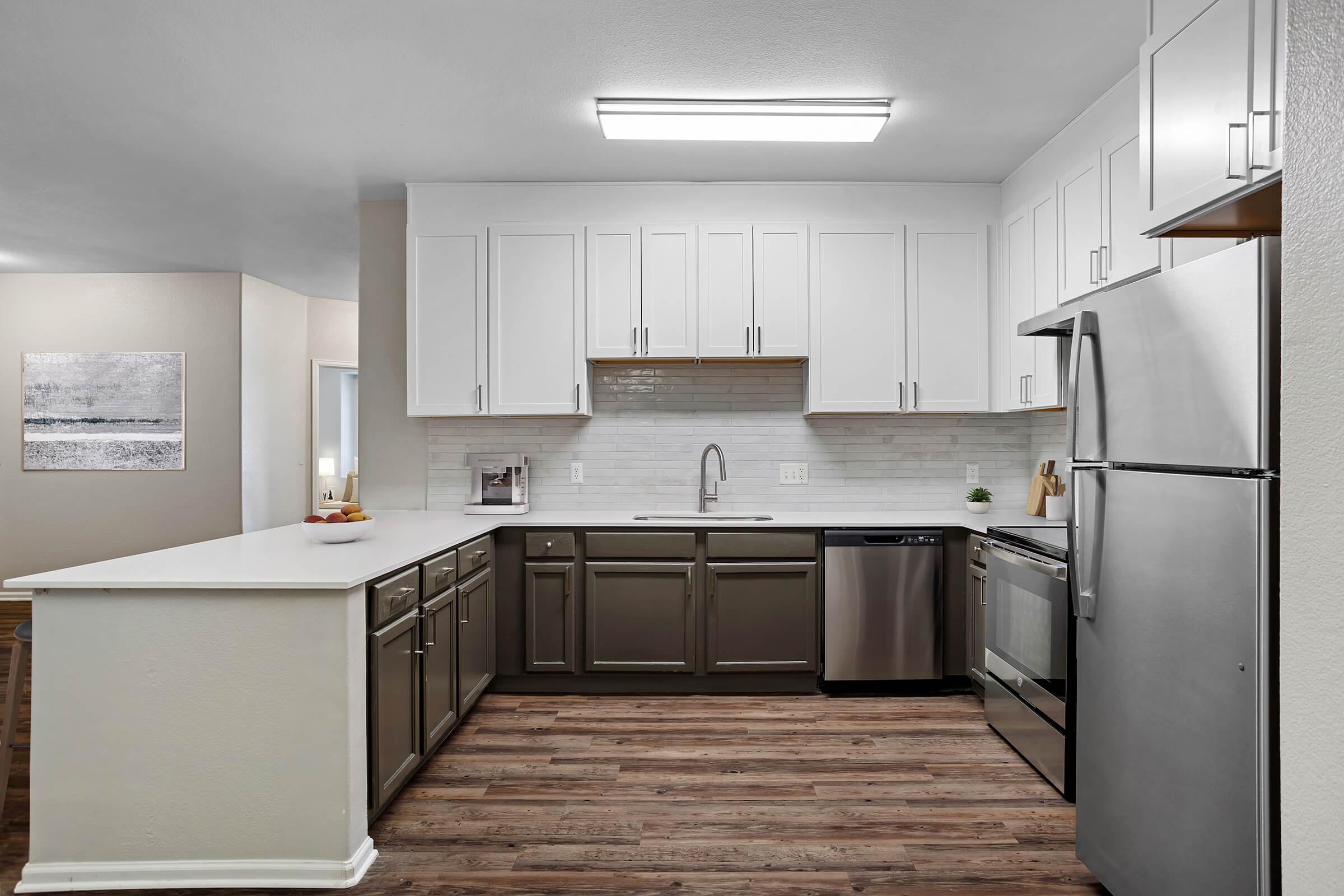 Modern kitchen with white cabinetry, stainless steel appliances, and a spacious countertop. The design features a mix of dark and light colors, including a light backsplash and wooden floor. A small decorative plant is placed next to the sink, enhancing the contemporary aesthetic.