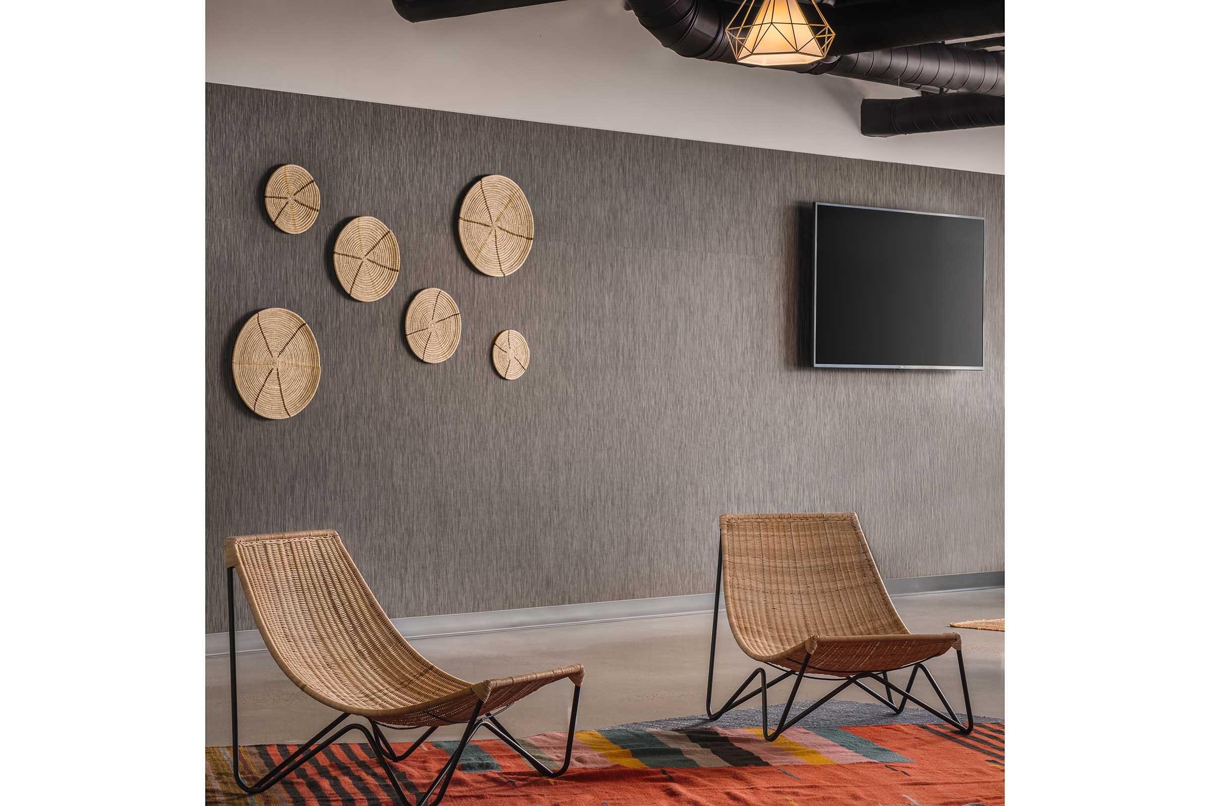 A modern interior featuring two woven chairs positioned in front of a textured wall adorned with circular wall decor. A flat-screen TV is mounted on the wall, and a colorful geometric rug adds warmth to the space, creating an inviting and stylish atmosphere.