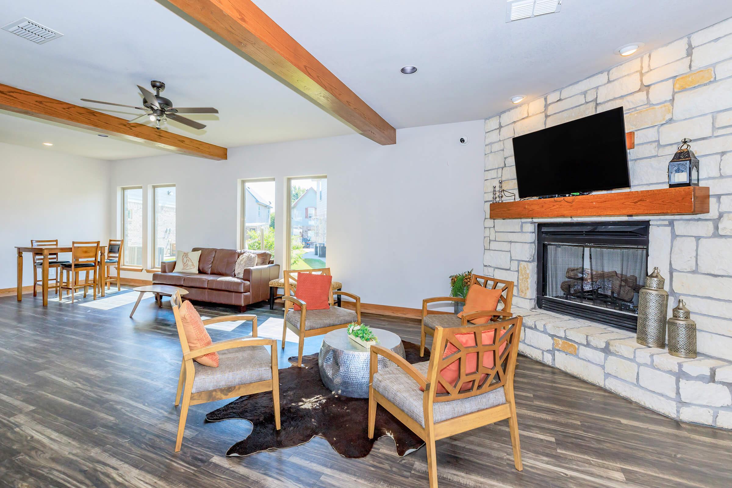 Spacious and modern living room with wooden beams, large windows, and a stone fireplace. Comfortable seating area with stylish chairs and a coffee table, complemented by decorative accessories. Includes a dining area with a table and chairs, creating a warm and inviting atmosphere.