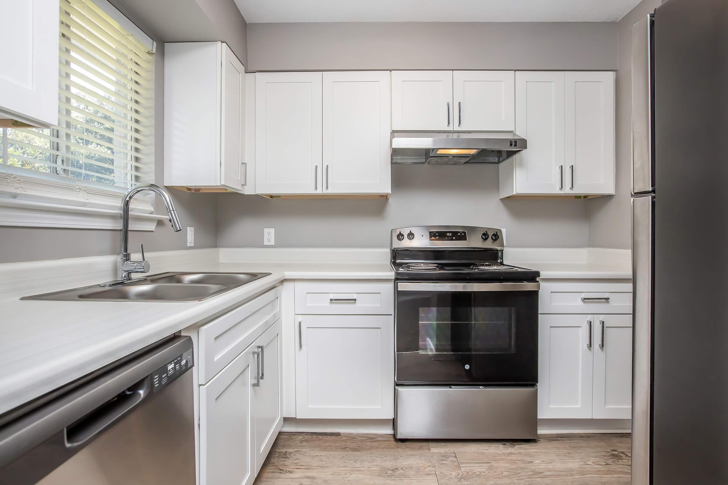 Modern kitchen featuring white cabinetry, stainless steel appliances, a built-in sink, and a sleek countertop. A window allows natural light to fill the space, and wooden floors add warmth to the design. The layout is functional and contemporary, ideal for cooking and entertaining.