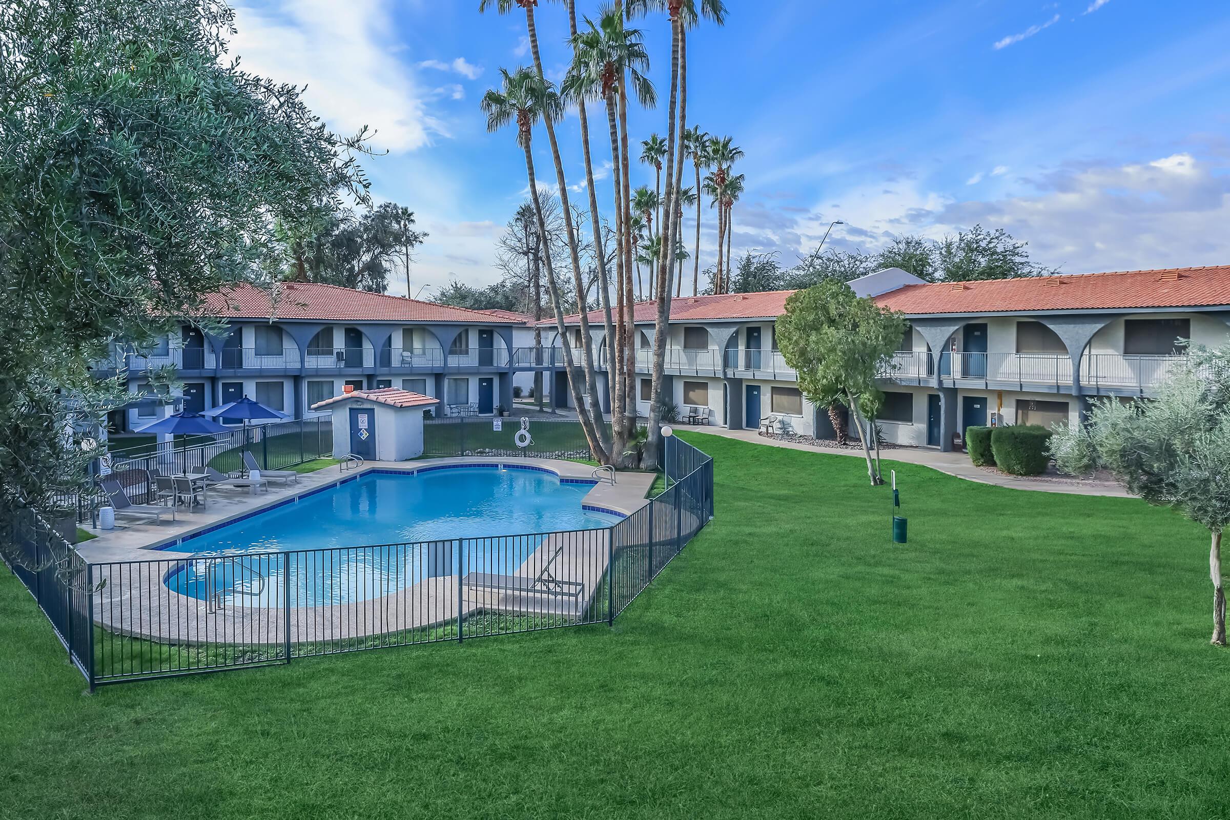 Aerial view of a fenced in outdoor pool surrounded by grass and a 2 story apartment complex