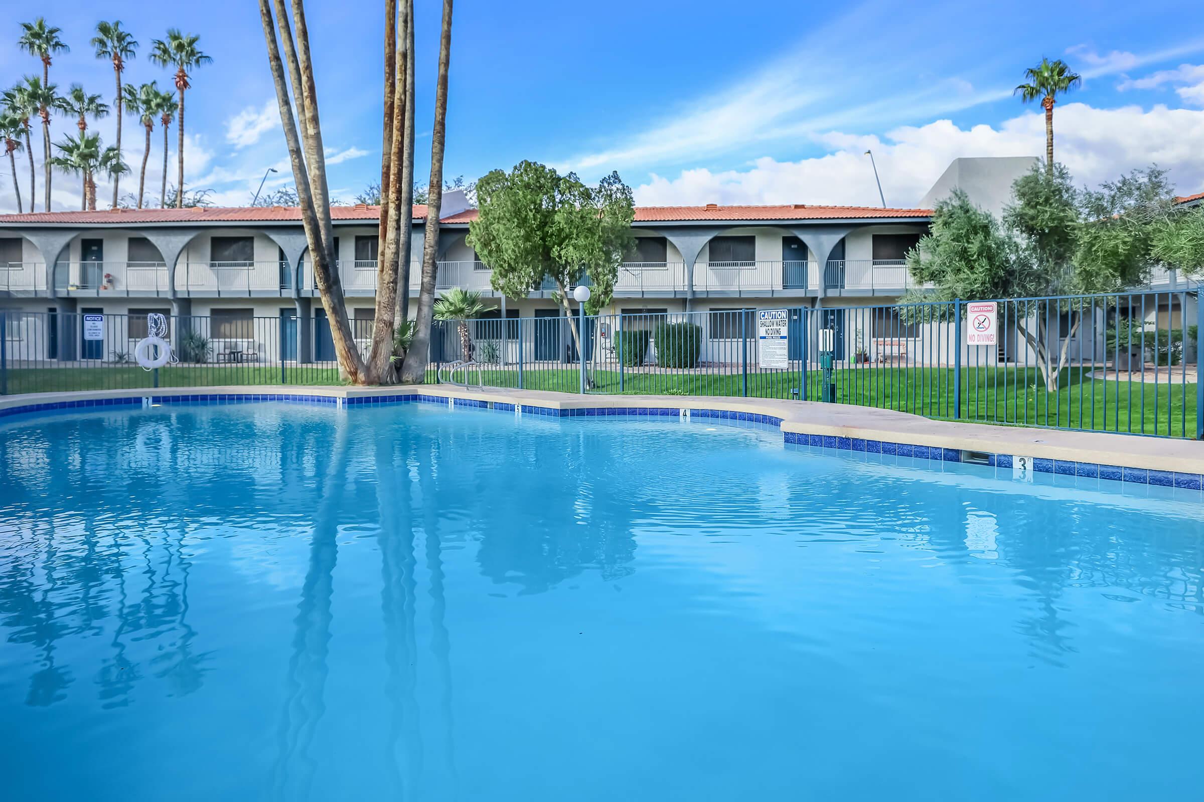 Large outdoor pool with view of a 2 story apartment building behind it