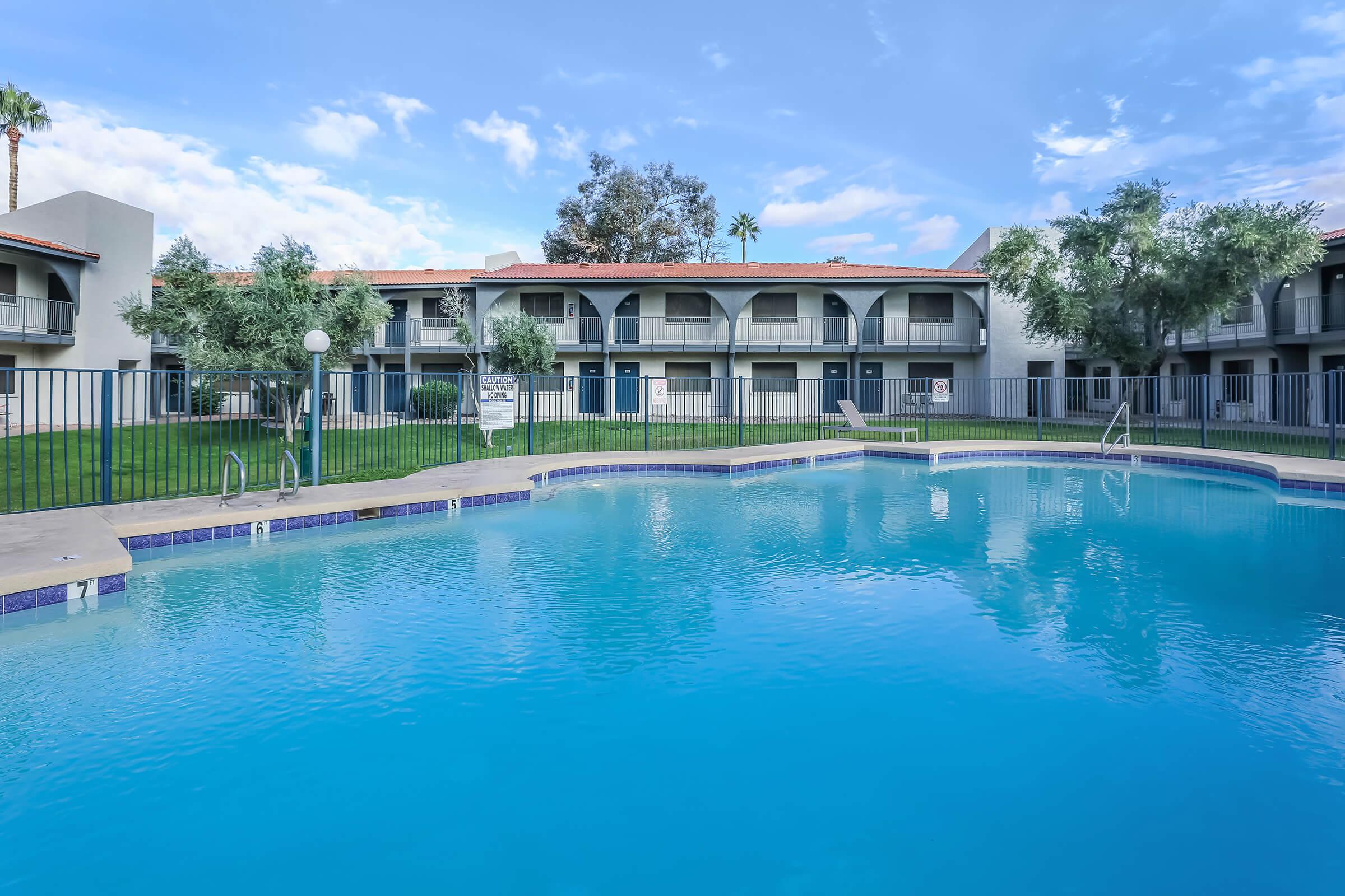 Large outdoor pool with view of a 2 story apartment building behind it